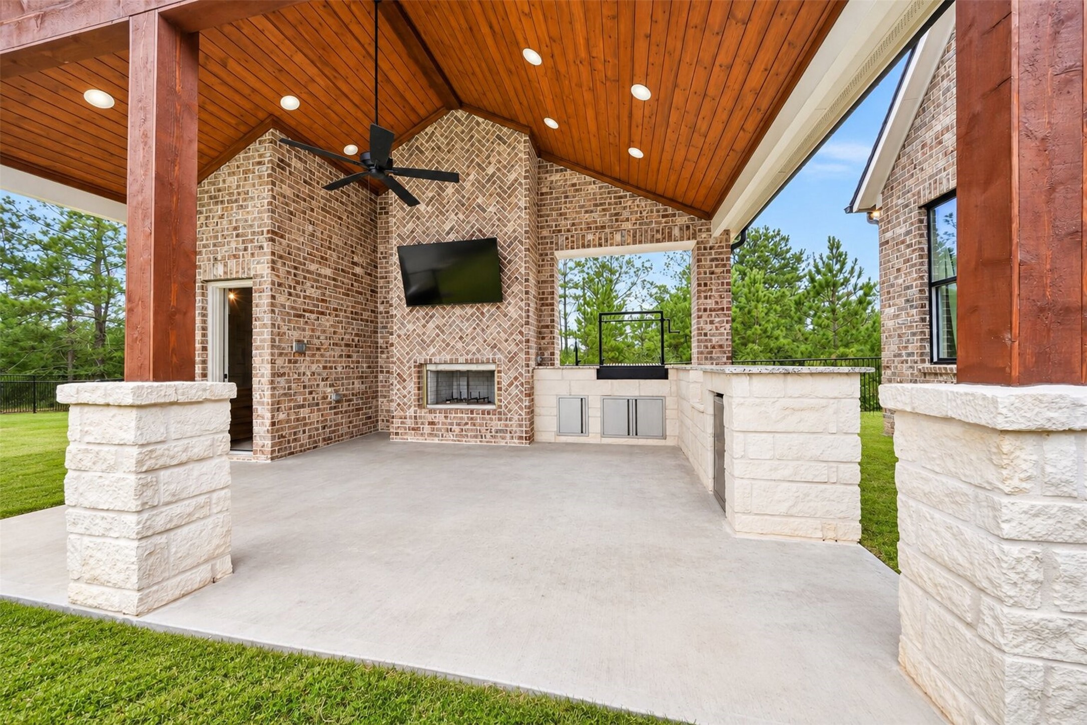 Timber posts frame the covered outdoor kitchen, where a brick fireplace and stone counters extend the home's entertaining space.