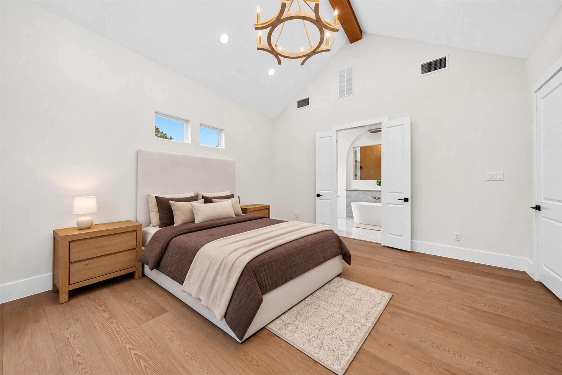 A vaulted ceiling and exposed wood beam give the primary bedroom an airy scale, with a doorway leading directly to the bath.