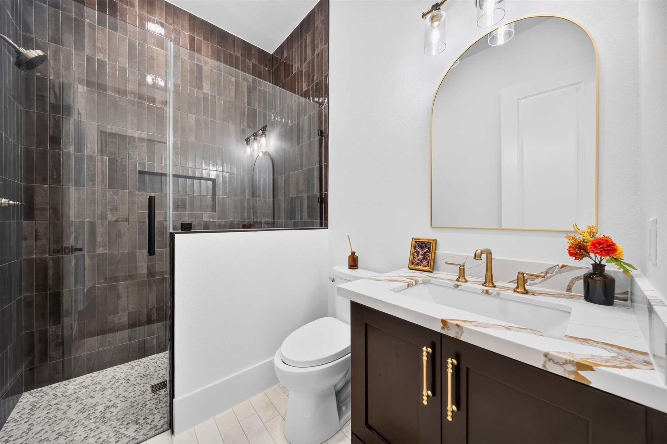 A glass-enclosed shower lined in dark tile contrasts with the light counter and double vanity for a crisp, balanced finish.