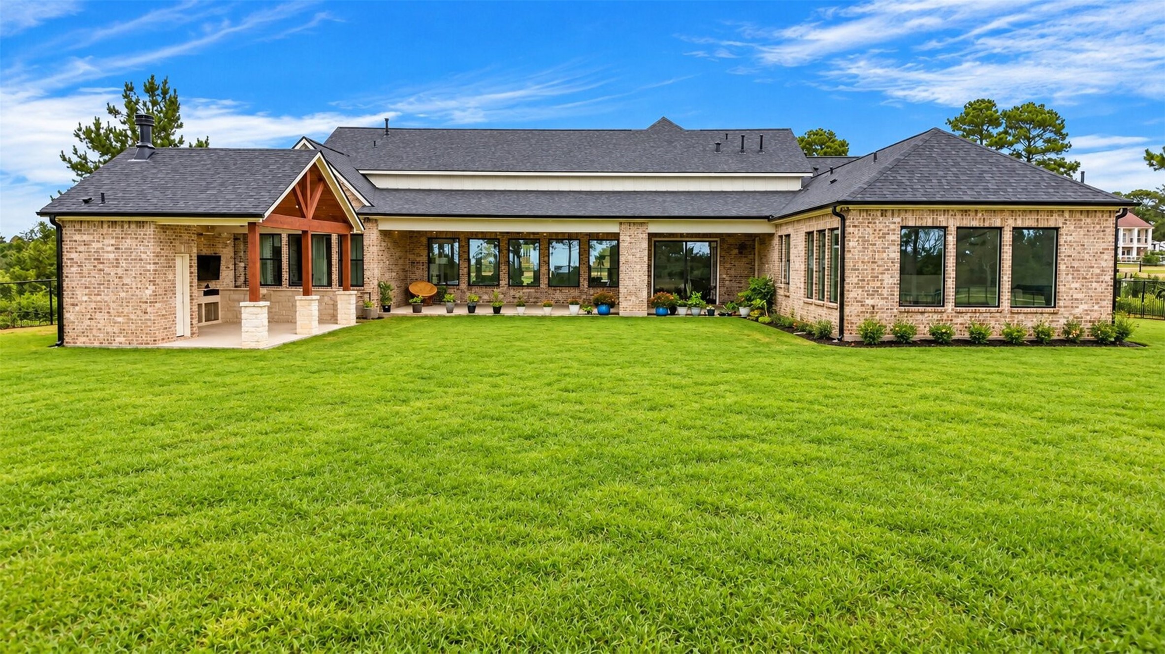 The rear brick elevation opens onto the covered patio, where timber framing shelters the built-in outdoor kitchen.