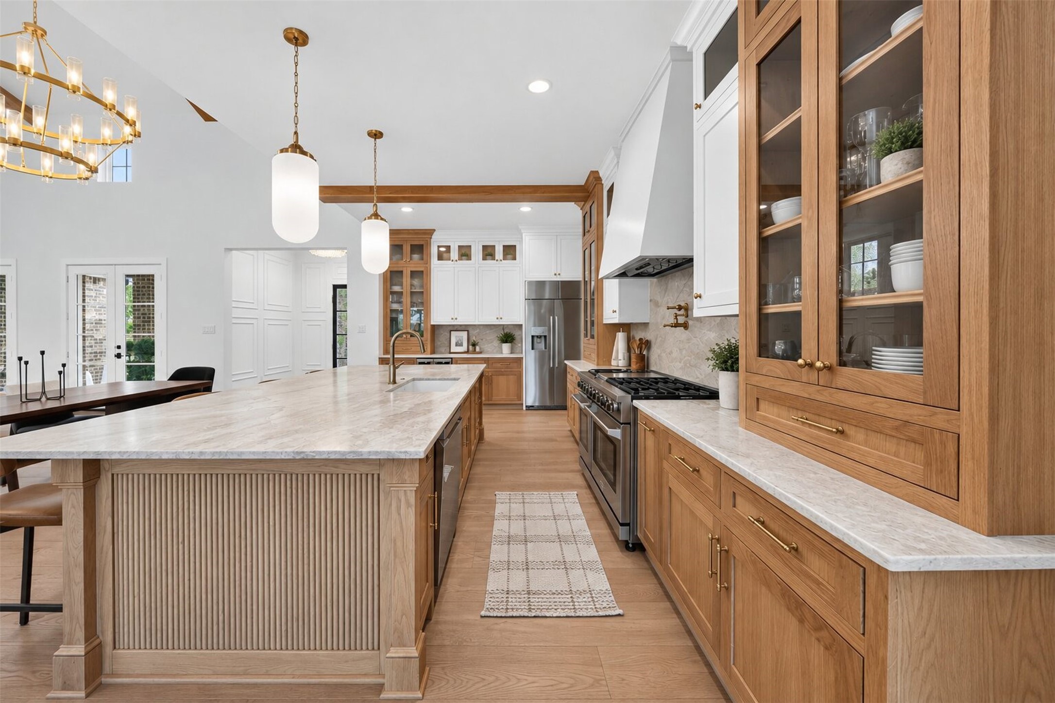 A broad vent hood draws the eye to the cooking wall, with patterned tile and warm wood cabinetry framing the gas range.