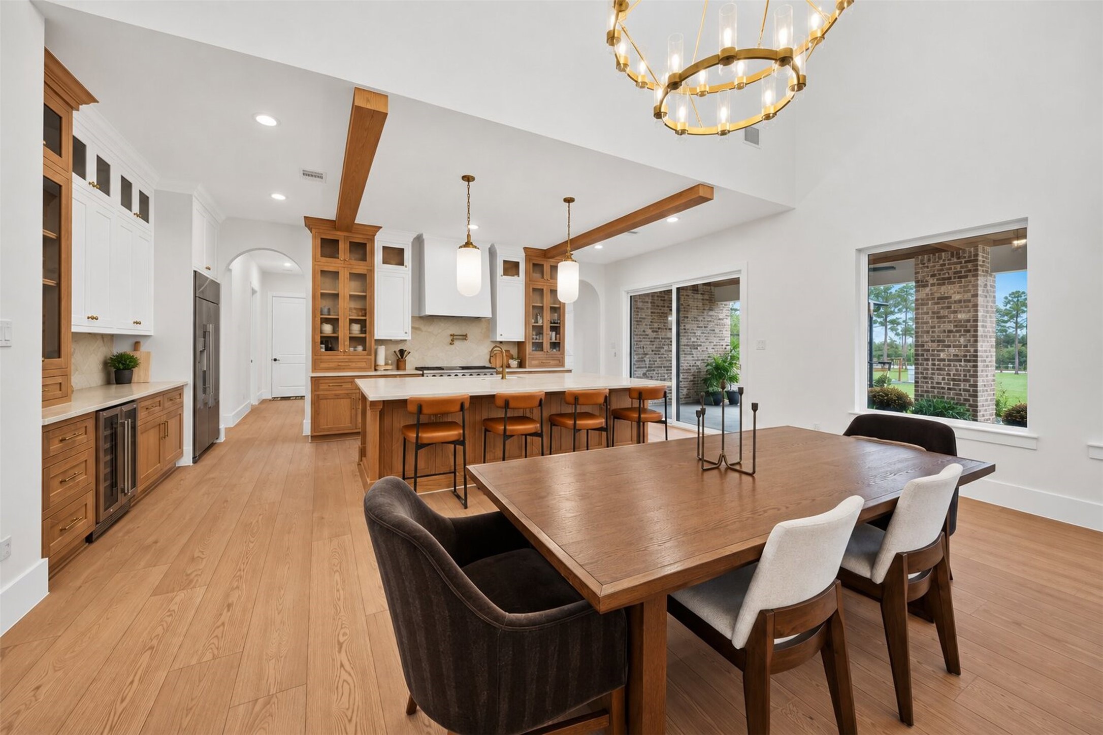 The kitchen opens to the dining area, with a stone island and warm wood cabinetry beneath exposed beams that tie both spaces together.