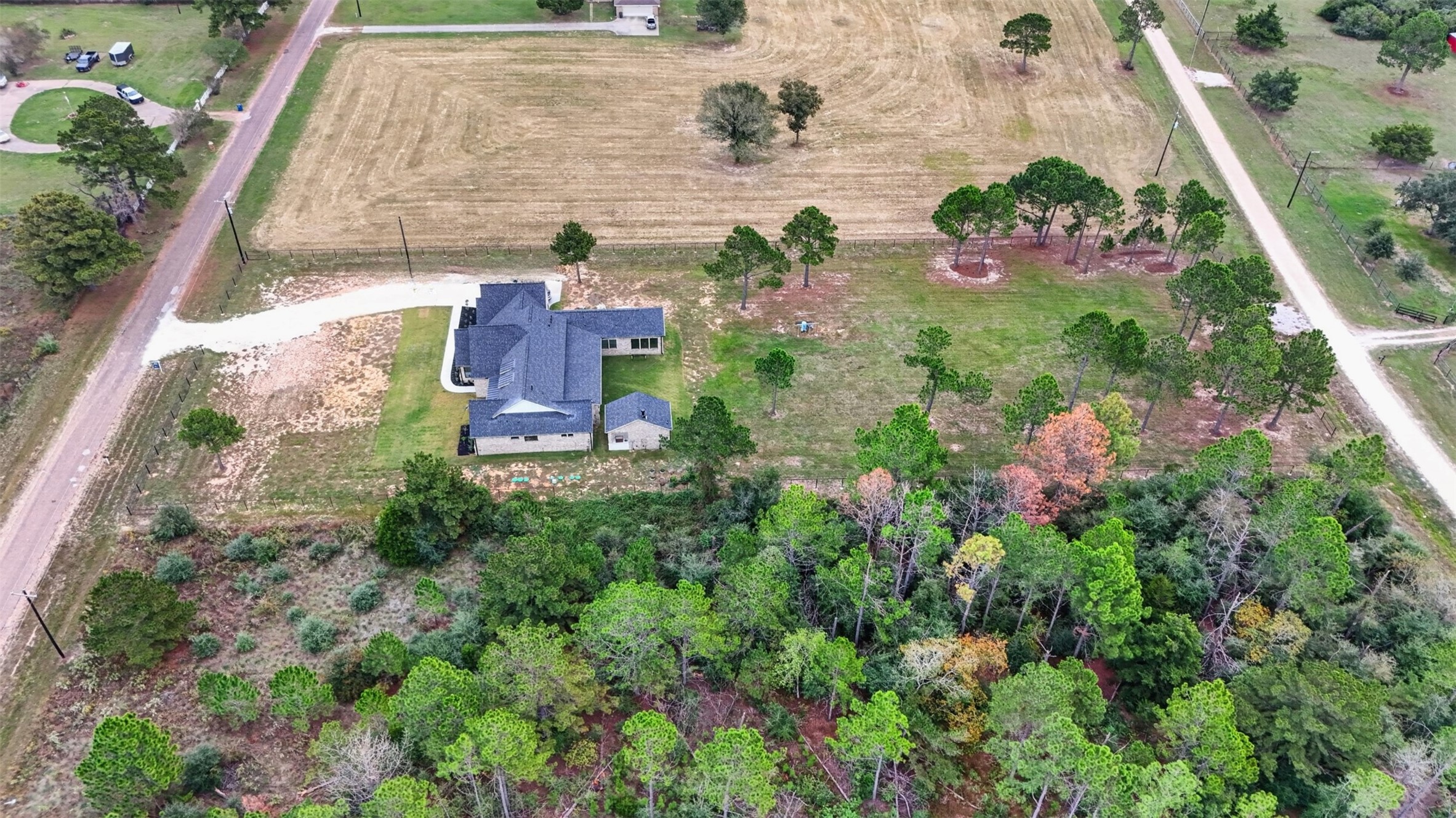The overhead view reveals the home's layered rooflines, with open acreage and surrounding trees extending beyond the house.