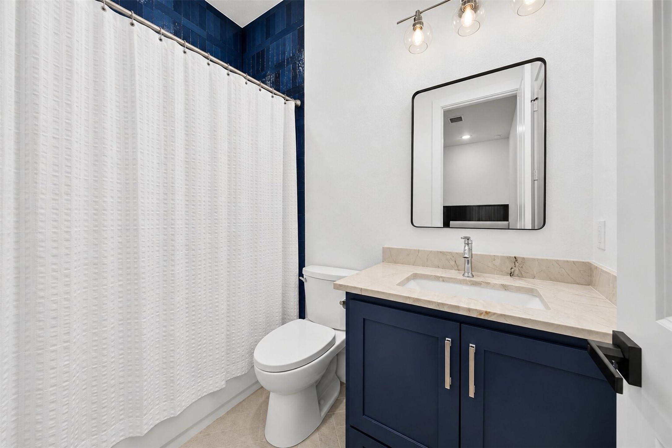 A navy vanity and blue tile accent bring color to this bath, balanced by pale counters and light flooring.