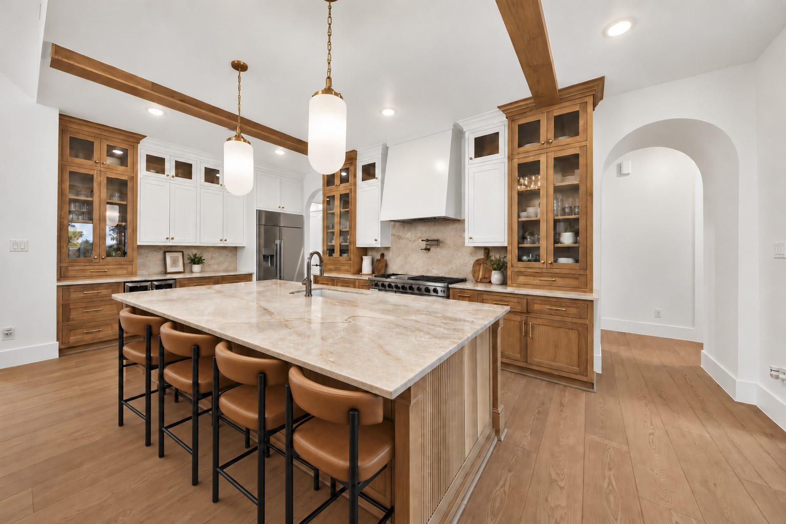 Glass-front wood cabinets surround a broad stone island, while the range and patterned backsplash anchor the kitchen's cooking area.