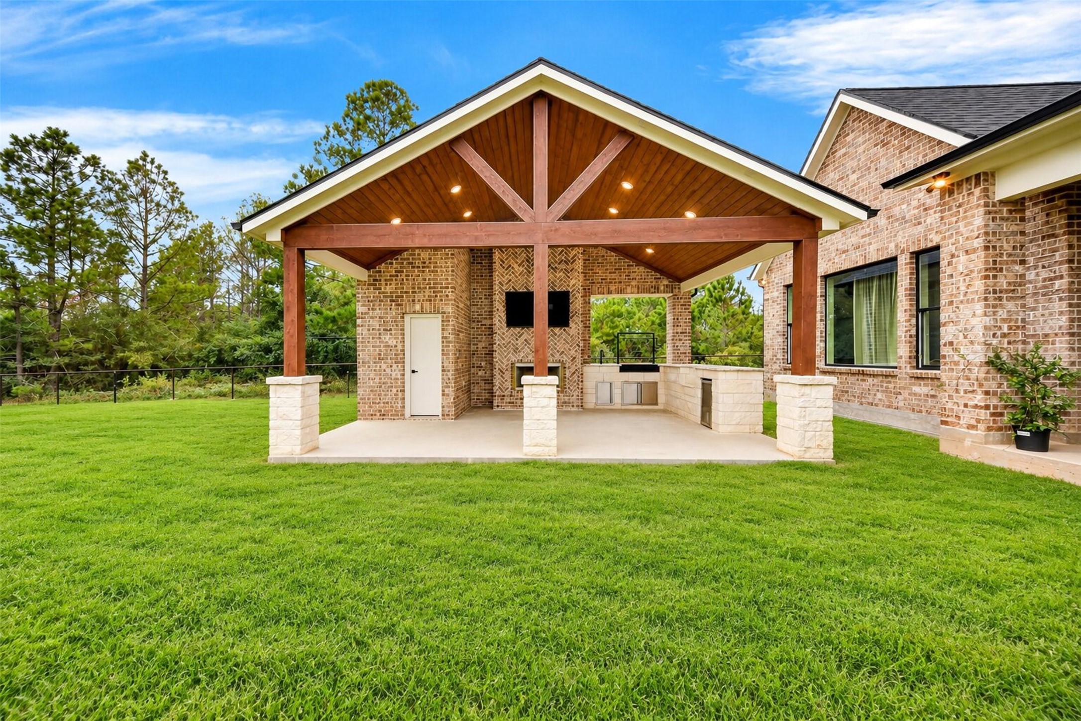 A timber-framed gabled pavilion shelters the outdoor fireplace and kitchen beside the broad backyard lawn.