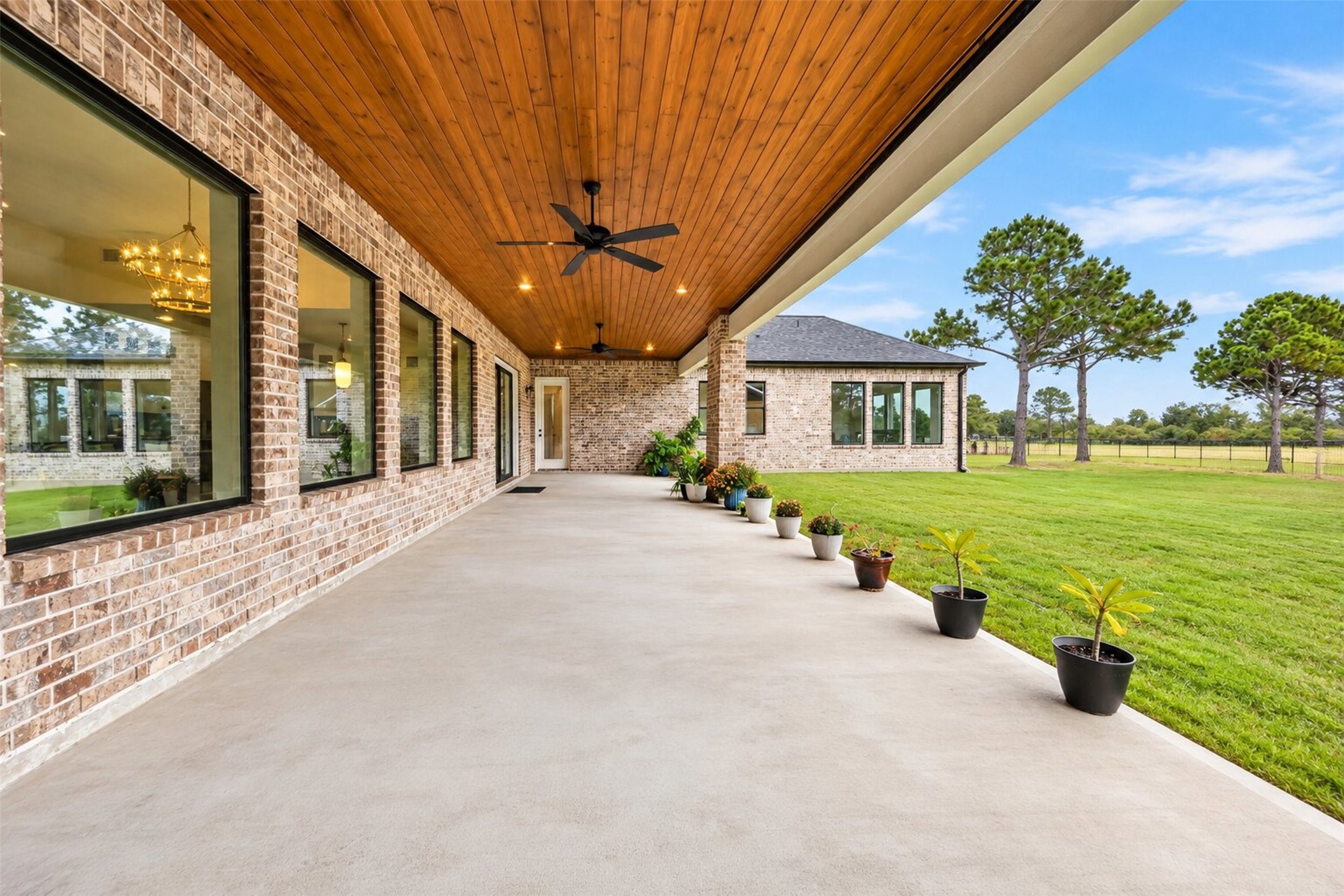 A long covered patio runs along the rear of the home, with a wood-plank ceiling and open views across the backyard lawn.