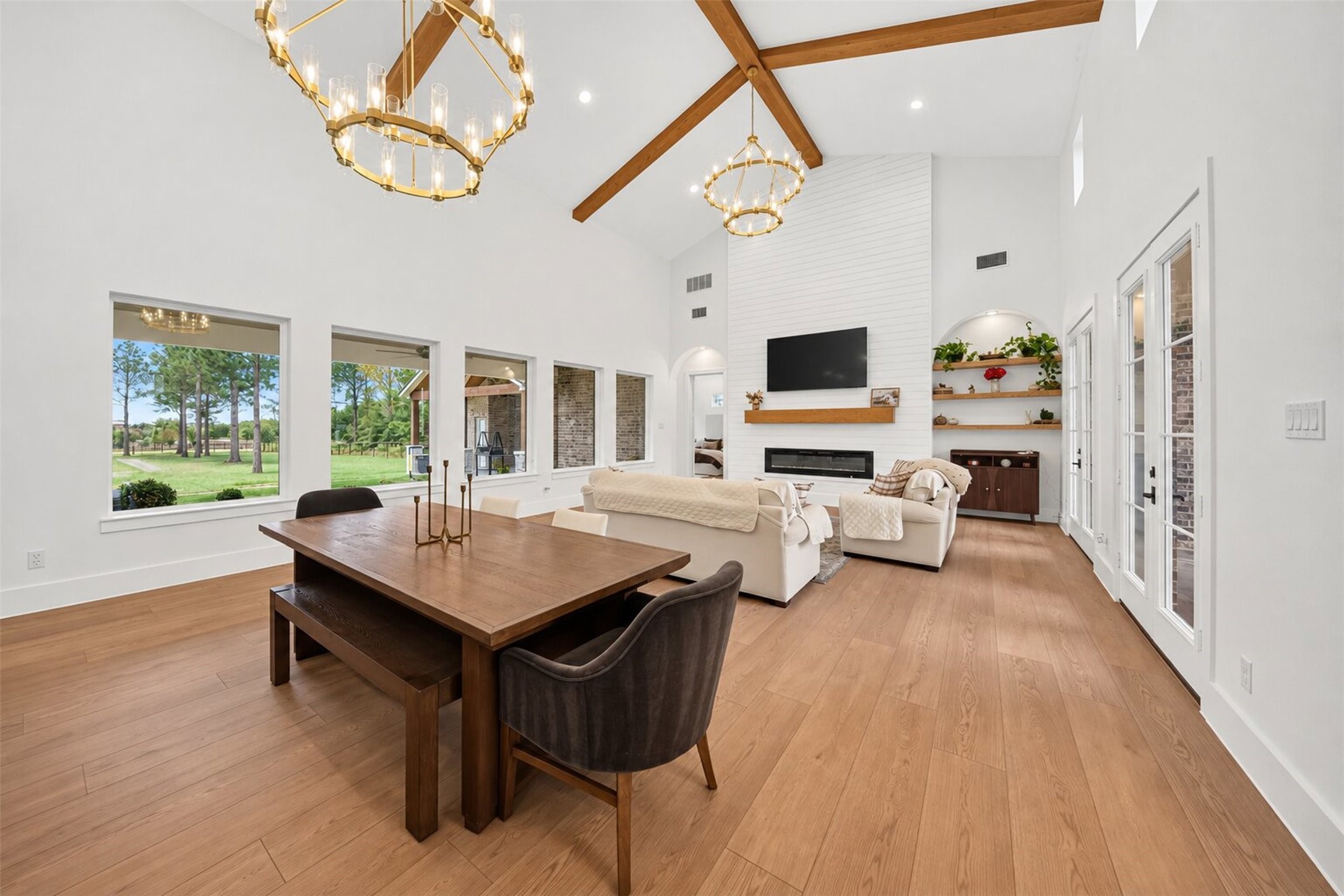 Exposed wood beams cross the vaulted great-room ceiling, while tall windows and a shiplap fireplace wall give the space an airy feel.