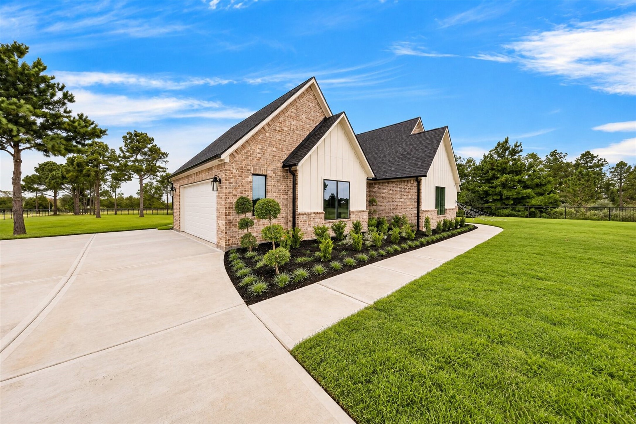 The long concrete drive follows the side elevation, with low planting and mature trees softening the brick exterior.