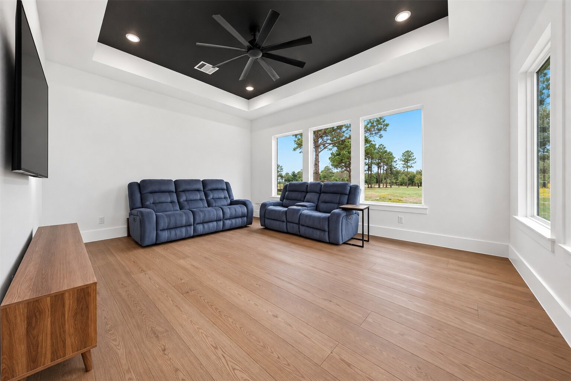 A dark tray ceiling defines the game room, while broad windows bring in natural light and views of the surrounding property.