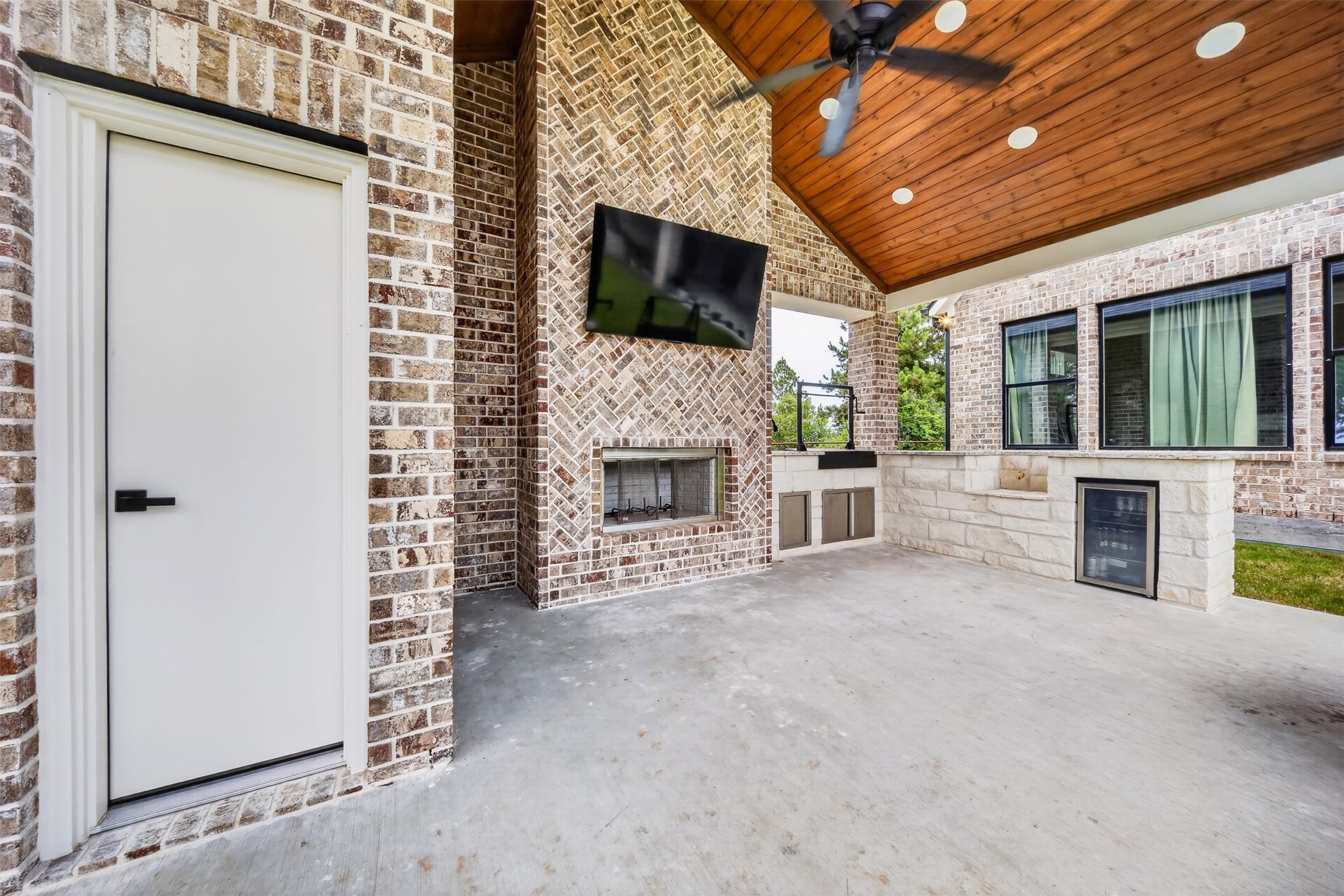 The outdoor kitchen pairs stone counters with a brick fireplace wall, all sheltered beneath the covered patio's wood-plank ceiling.