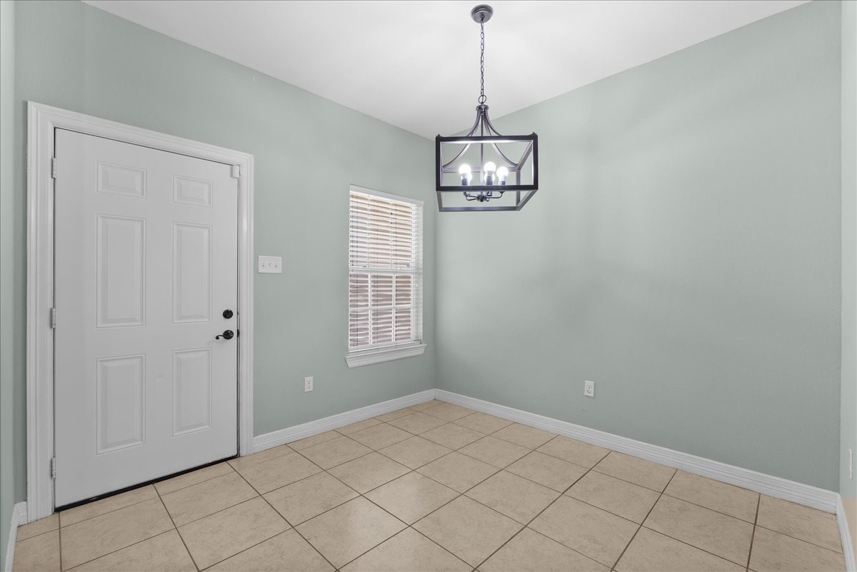 A statement chandelier marks a defined dining space just off the kitchen, framed by a nearby window and a convenient door leading out to the yard. Tile flooring, crown molding, and fresh neutral paint carry the home's finishes through to this corner of the main living area.