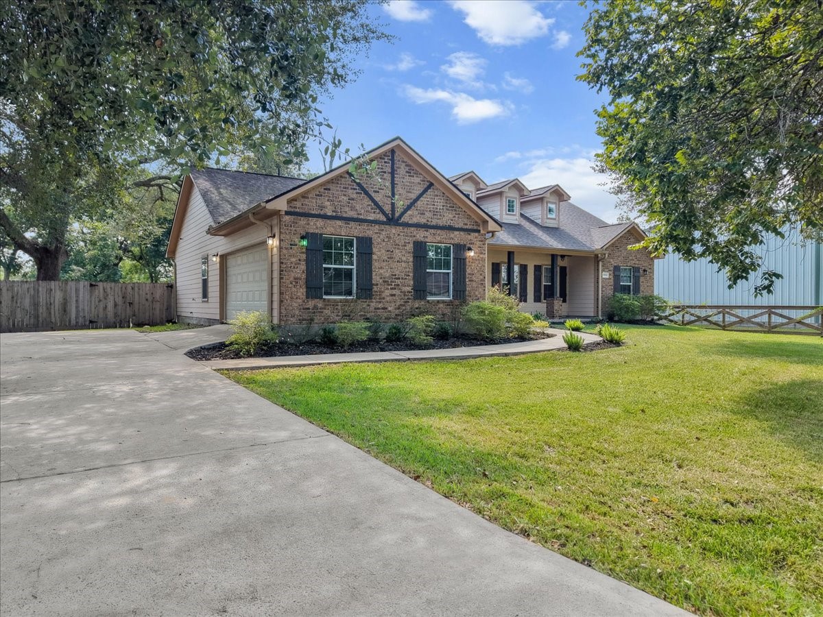 A generous double-wide driveway sweeps up beneath towering oaks, giving this brick craftsman-style home plenty of curb presence from the street. The open lawn and fenced side yard hint at the space and privacy that continue throughout the property.