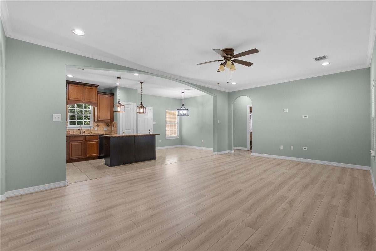 An expansive open-concept floor plan links the living space to the kitchen through a wide archway, with pendant lighting over the island and a chandelier marking a defined dining area.
