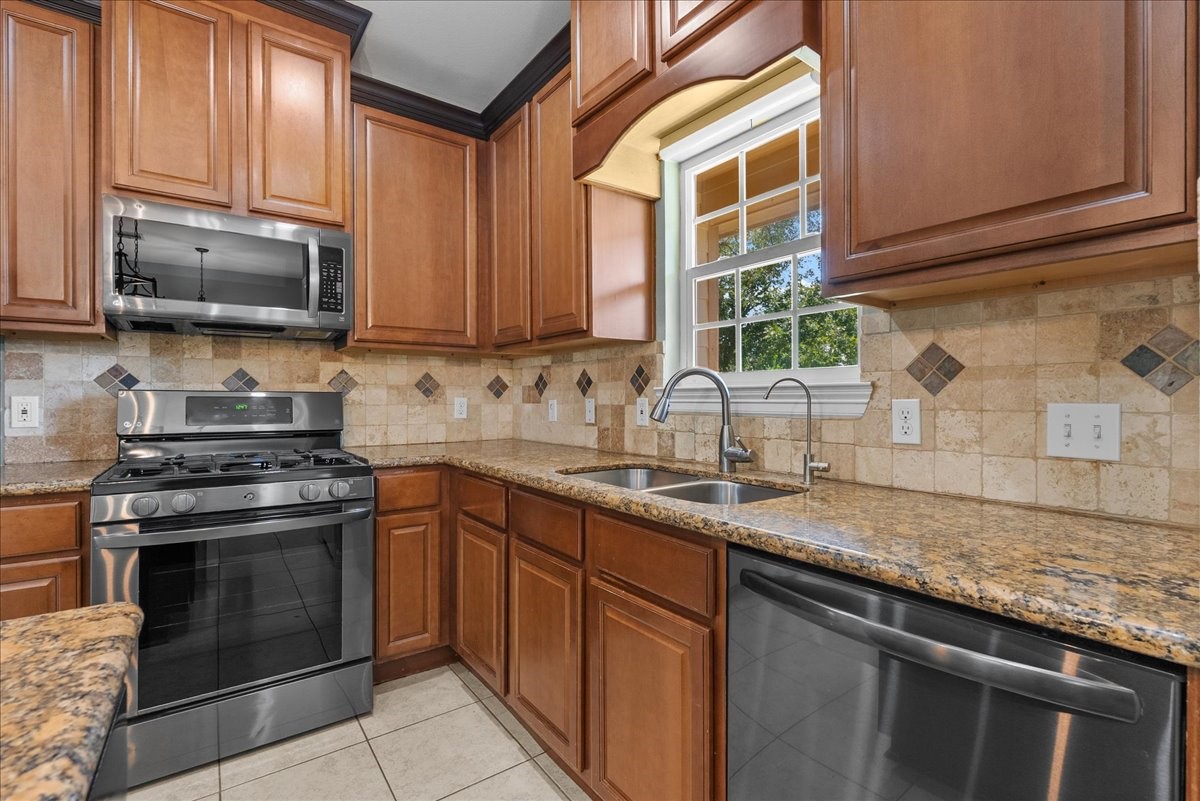 An arched window frame above the sink brings in natural light and backyard views, paired with a gooseneck faucet and side sprayer. Granite counters wrap the L-shaped layout, with a stainless dishwasher and additional cabinet and drawer storage rounding out the prep space.