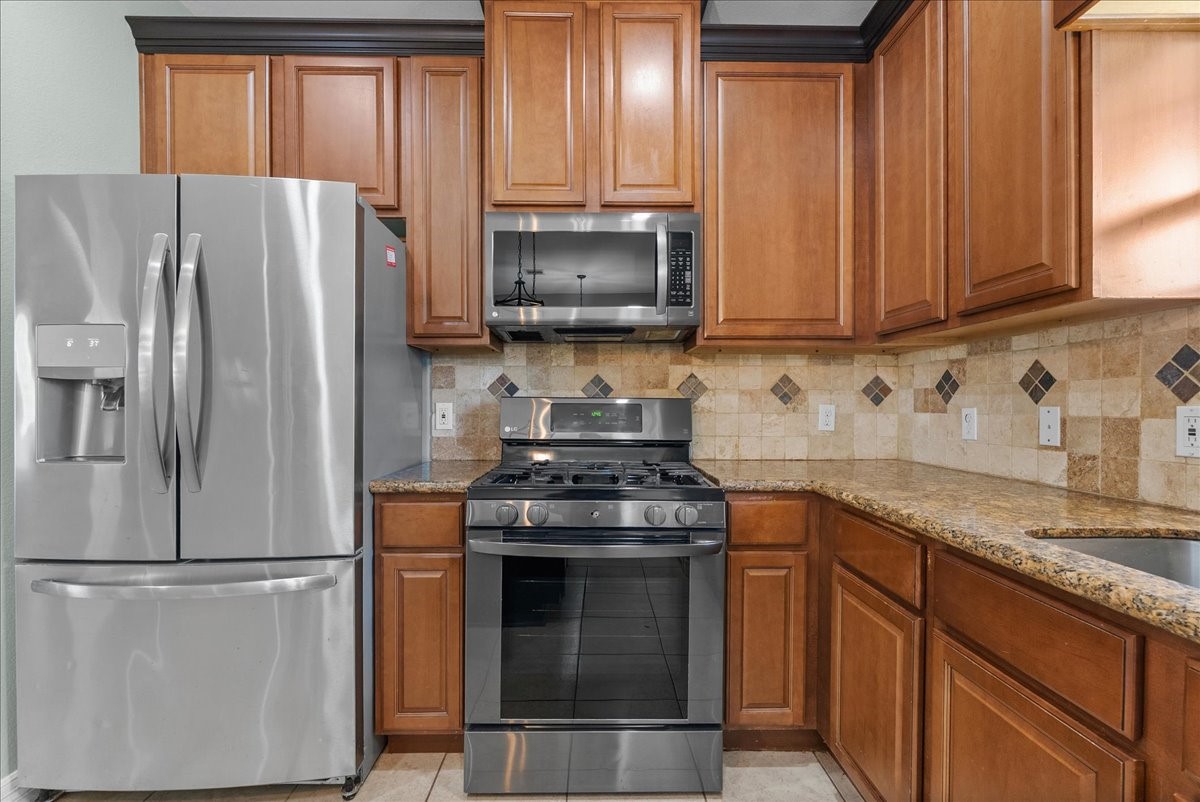 Stainless steel appliances, a French-door refrigerator with water/ice dispenser, over-the-range microwave, and LG gas range, sit against rich wood cabinetry and granite countertops. A diamond-patterned tile backsplash and matching floor tile add a polished, cohesive finish to the space.