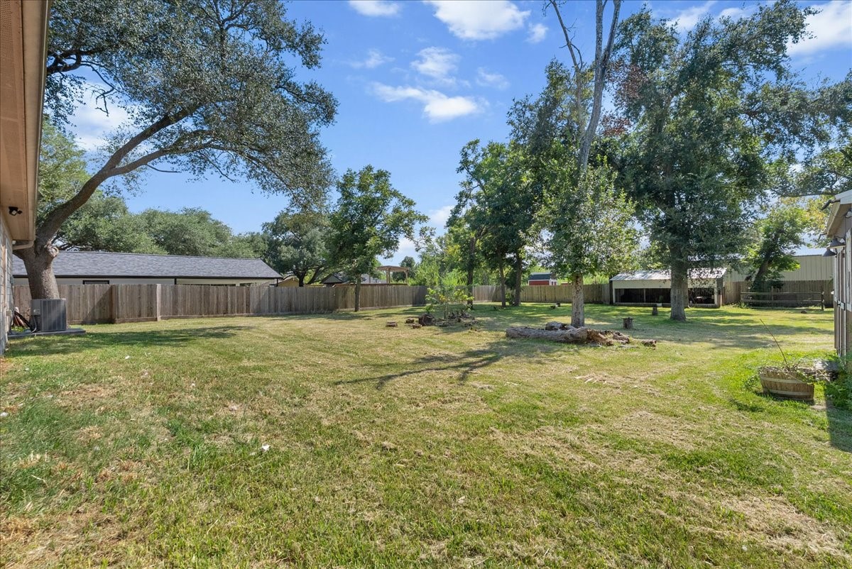 The fully fenced backyard offers a wide, open expanse of grass shaded by mature oak trees.