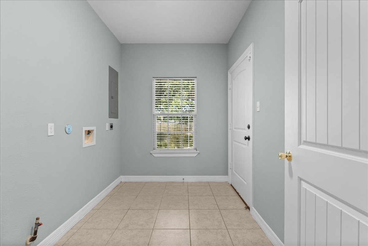 The spacious laundry room includes washer/dryer hookups, an electrical panel, and tile flooring, with a window bringing in natural light and a door leading out to the garage.