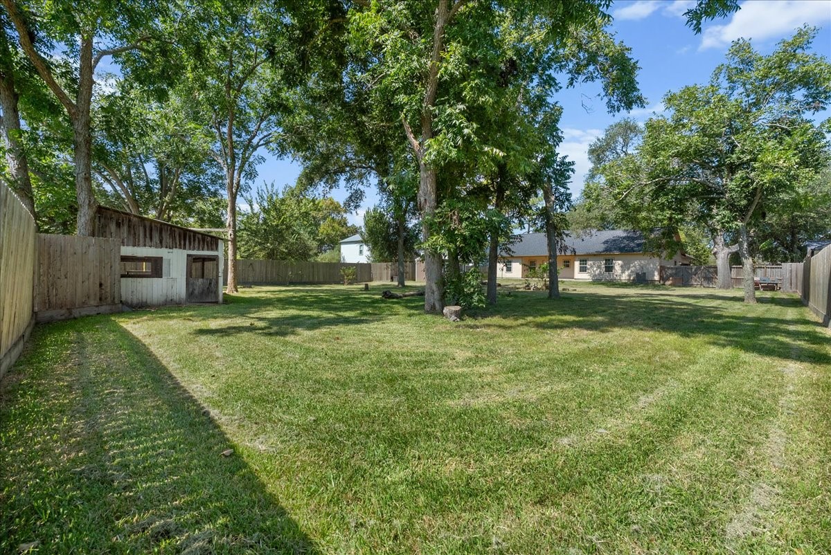 The fenced half-acre lot really shows here, with a deep, wide-open stretch of yard reaching well past the home's footprint. A canopy of mature trees scattered across the grounds keeps the space shaded without crowding it, leaving plenty of open acreage for a garden, play area, or future outdoor project.