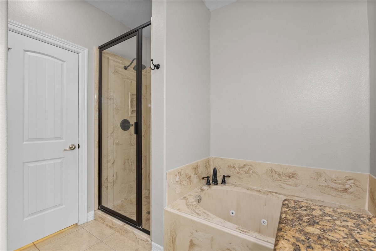 A frameless glass walk-in shower sits beside a separate garden tub with jets, both finished in coordinating marble-look surround. A private water closet door and granite countertop edge complete this spa-style ensuite.