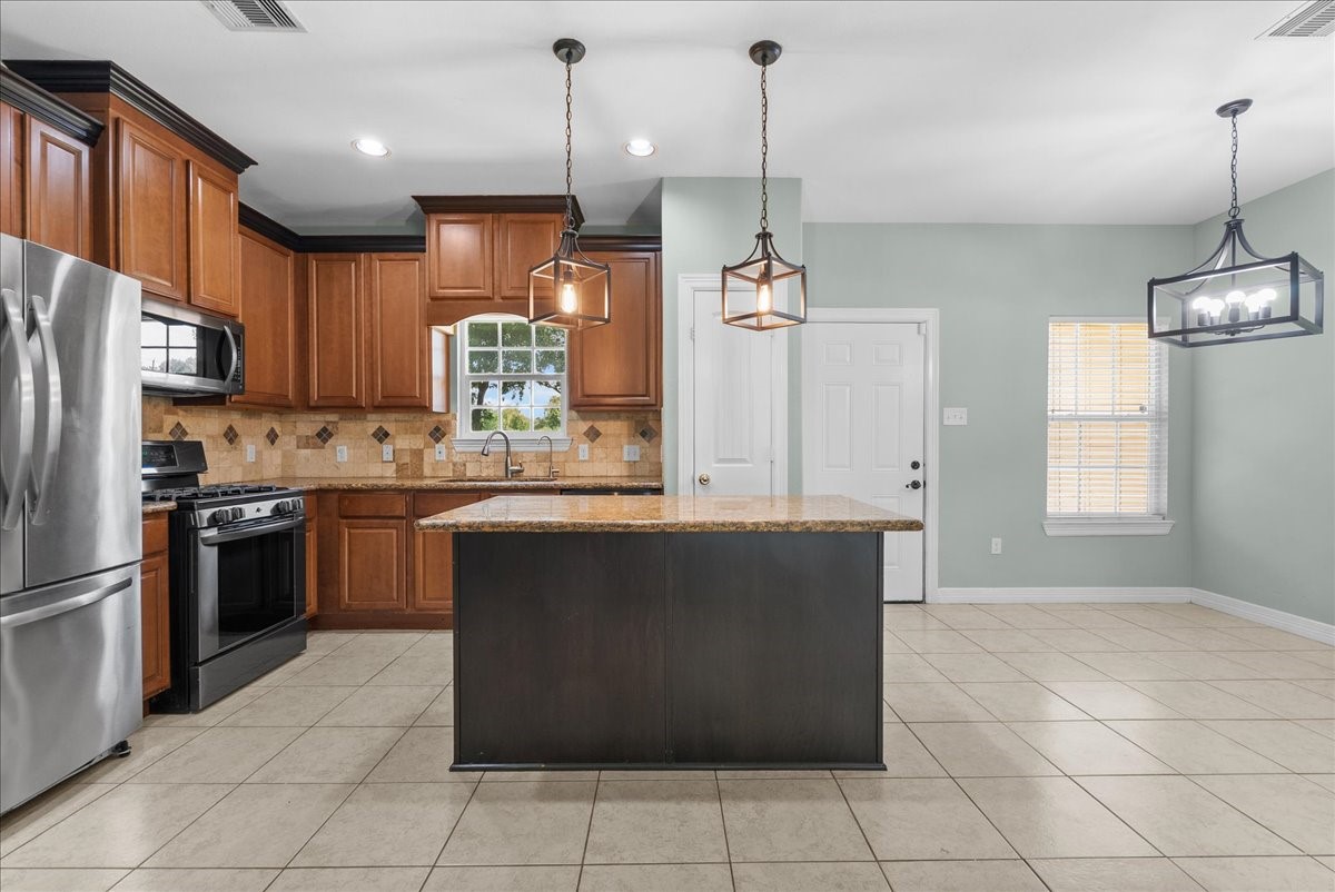 The kitchen is finished with granite counters, a tile backsplash, and a large center island with seating space, framed by three pendant lights overhead.