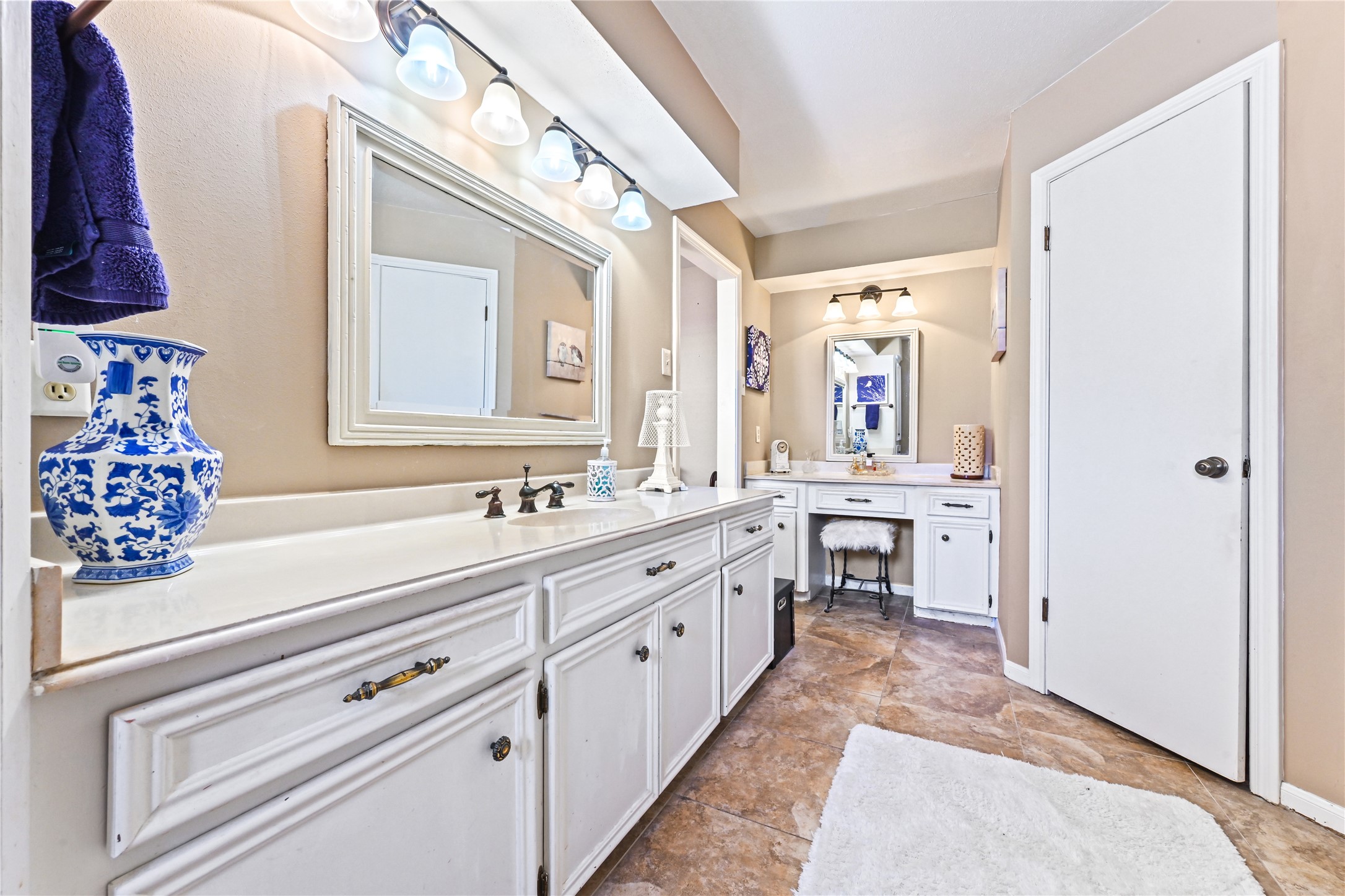 Spacious bathroom featuring dual vanities with elegant white cabinetry, stylish lighting, and a cozy makeup station for a luxurious touch.