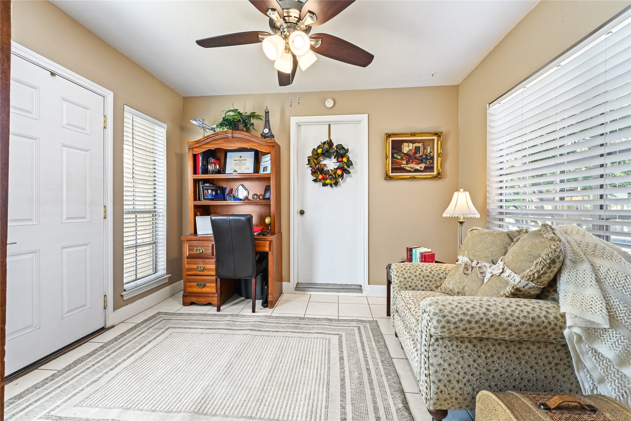 Charming and cozy sitting area features a plush armchair, a classic wooden desk with built-in shelves, and ample natural light from large windows, creating a warm and inviting space.
