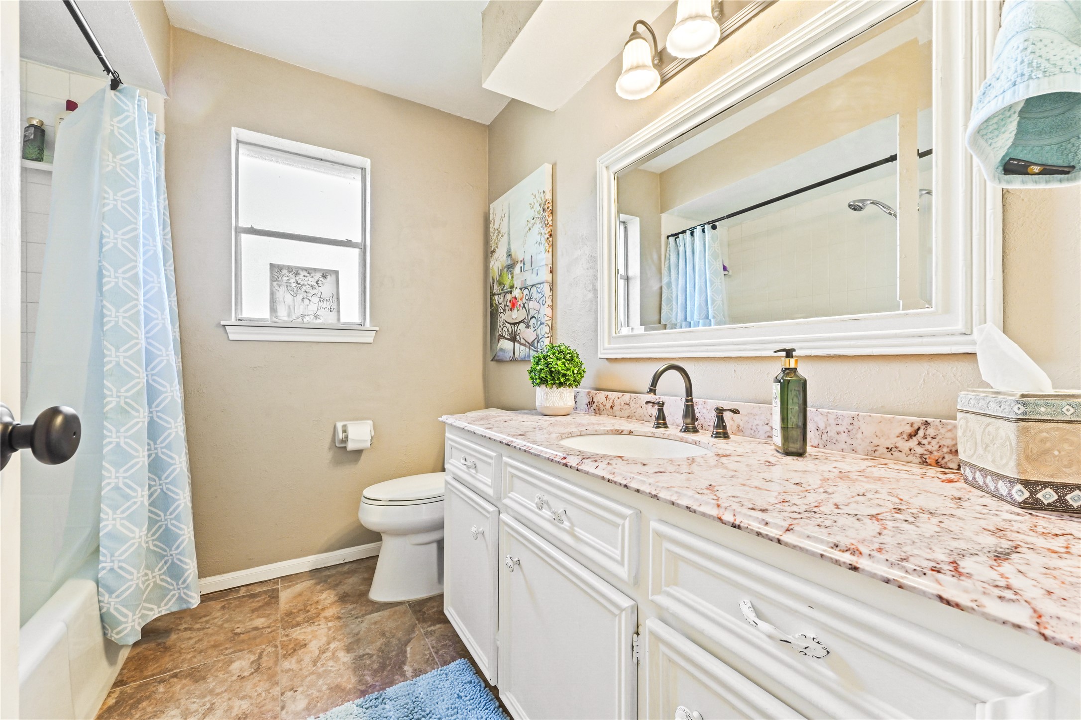 Bright and inviting bathroom featuring a spacious vanity with dual sinks, elegant granite countertops, and stylish fixtures. Natural light pours in through the window, enhancing the serene atmosphere.