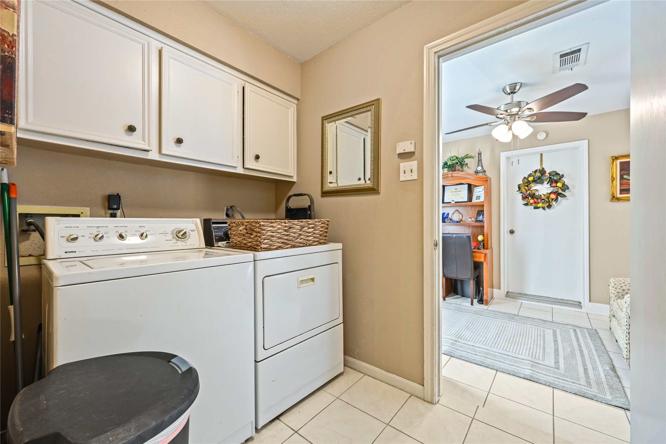 Convenient laundry room equipped with a washer and dryer, ample cabinetry for storage, and easy access to an adjoining room with a ceiling fan and office nook.