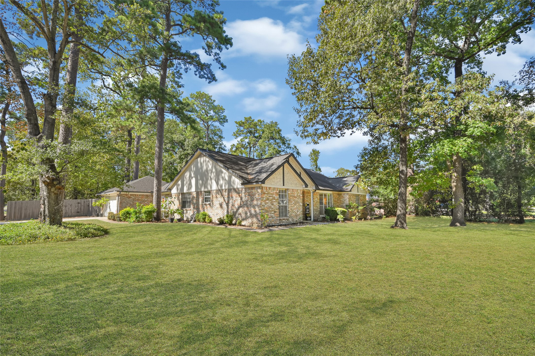 Charming brick home nestled among mature trees, offering a spacious and lush green lawn ideal for outdoor enjoyment.