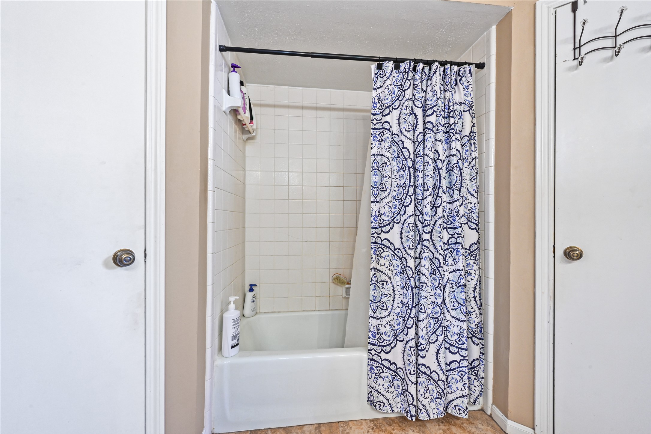 Cozy bathroom featuring a classic white tiled shower-tub combo with an elegant blue and white patterned curtain, offering a functional and stylish space.