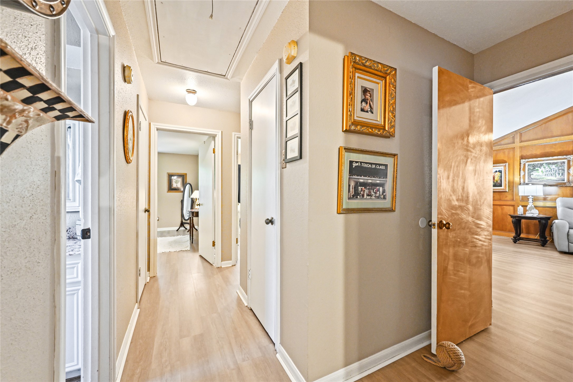 Bright hallway with light wood flooring, leading to multiple rooms. Adorned with framed artwork, it offers a warm and inviting transition to spacious living areas.
