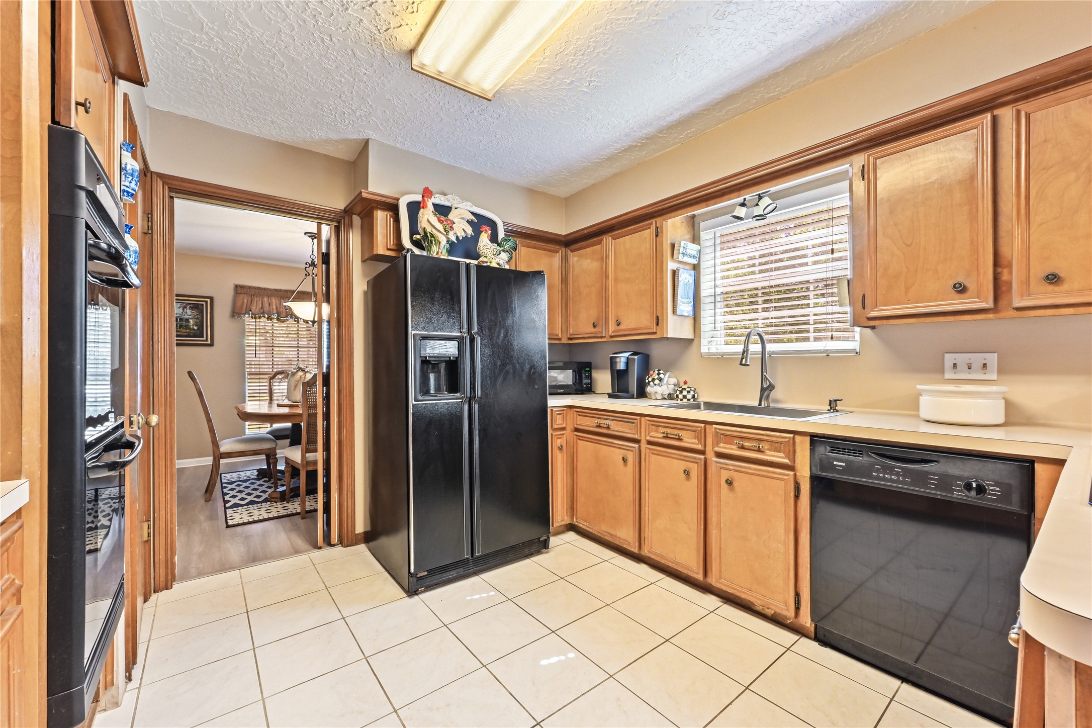 Charming kitchen with warm wooden cabinetry, sleek black appliances, and a cozy dining area just beyond, perfect for family gatherings.