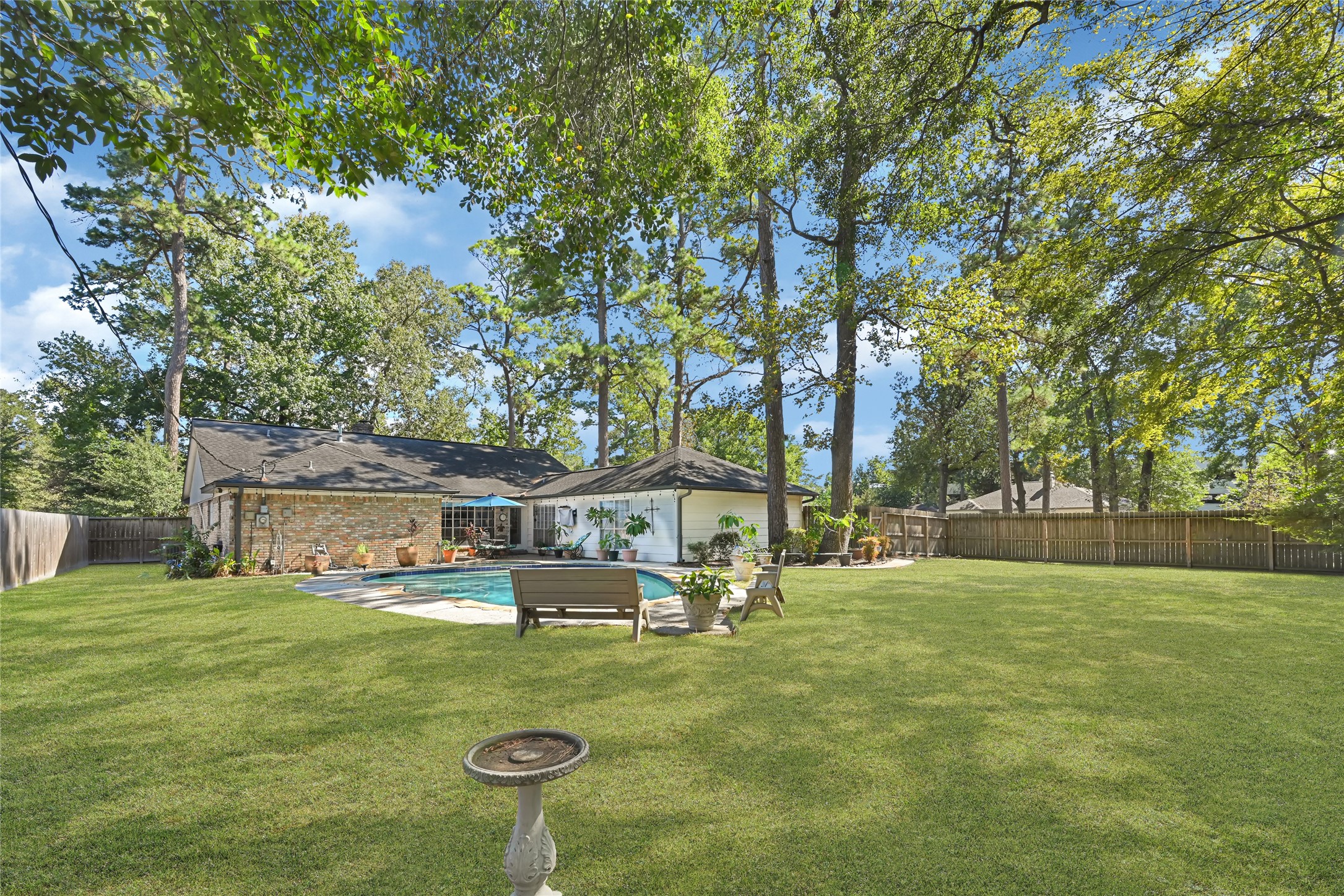 Expansive backyard oasis featuring a pristine pool surrounded by lush greenery and mature trees, ideal for outdoor relaxation and entertaining.