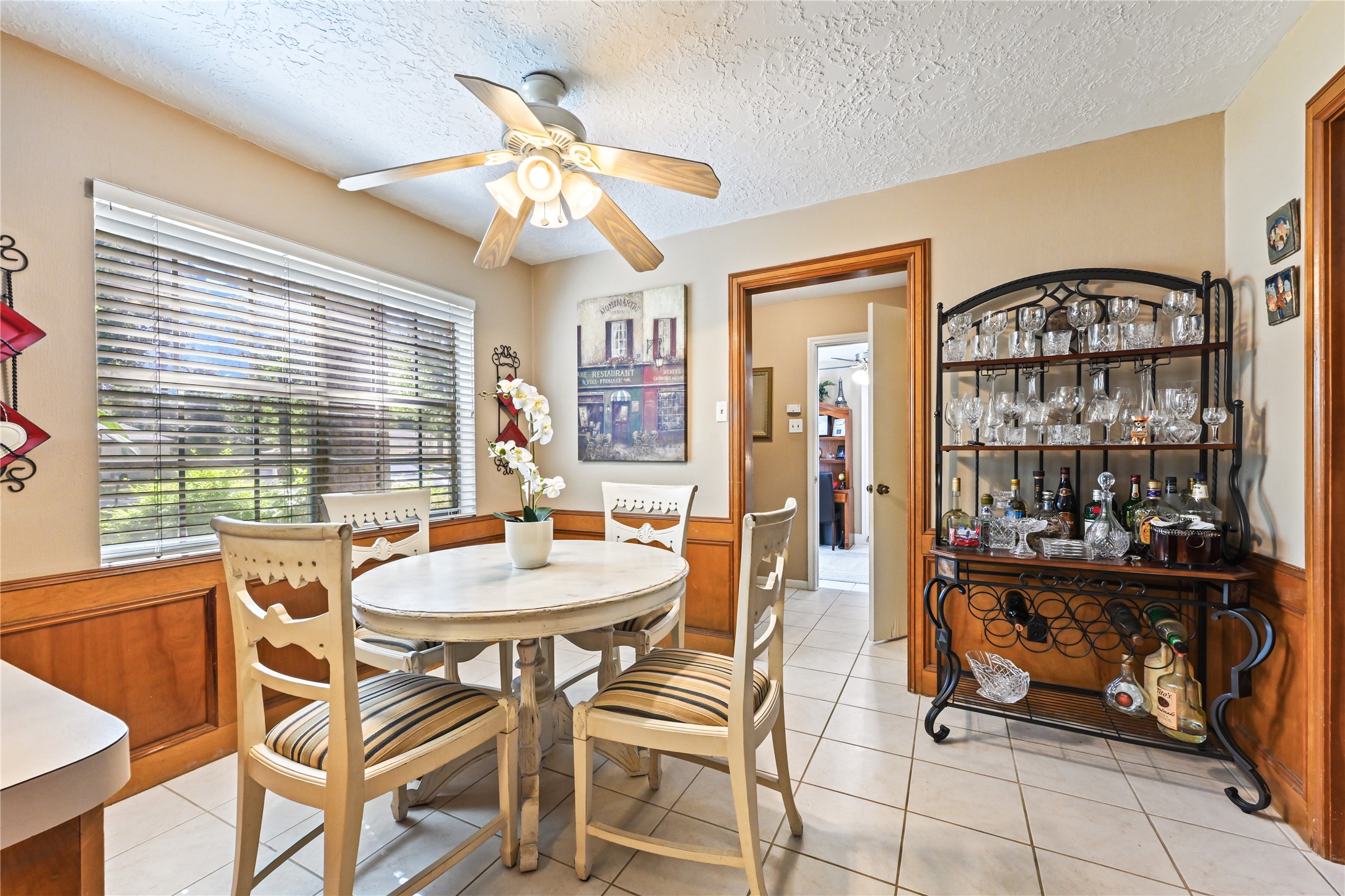 Cozy dining area with a round table and chairs, highlighted by natural light streaming through large windows. A ceiling fan and stylish bar cart add charm and functionality.