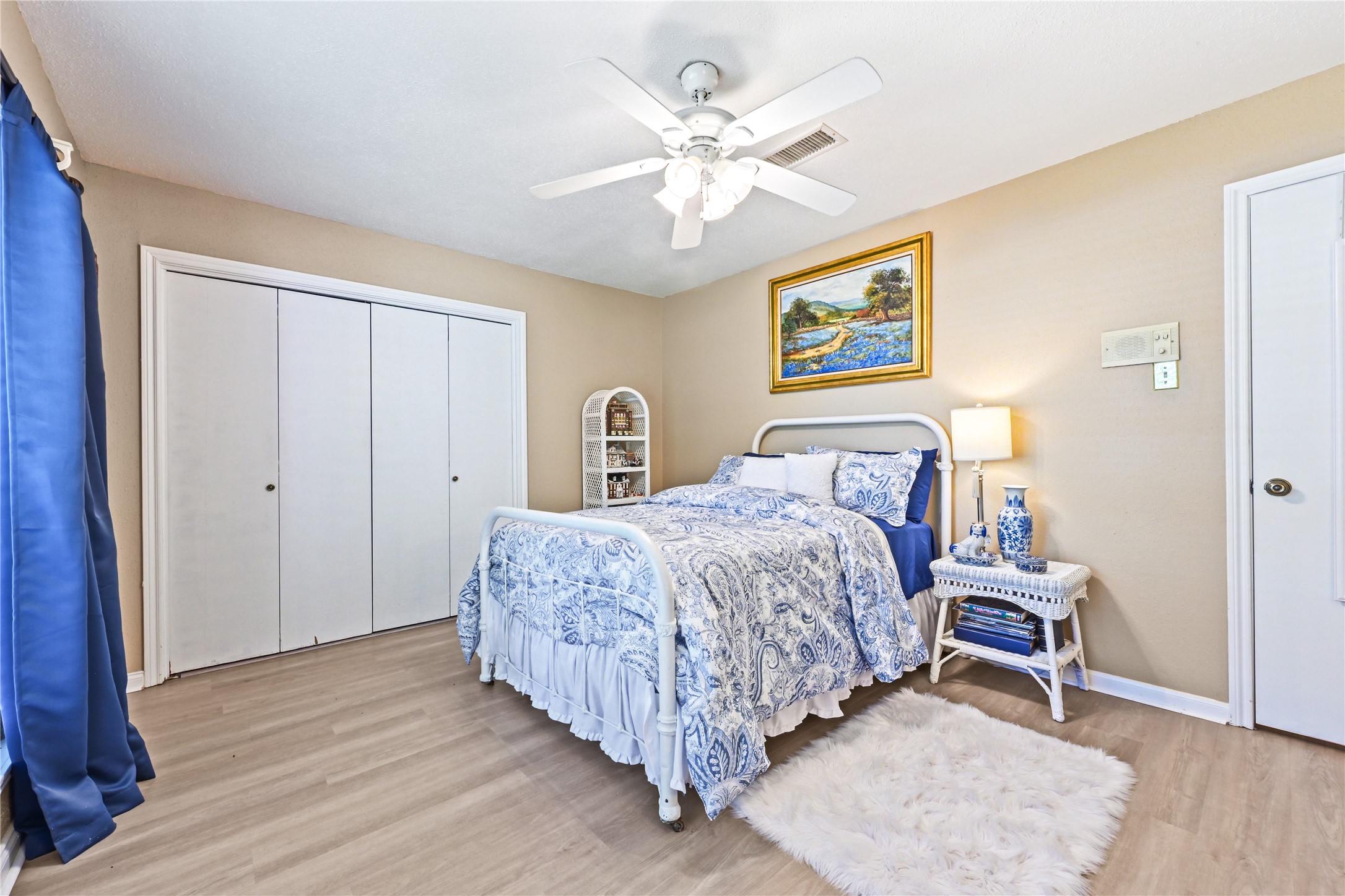 Charming bedroom with elegant blue and white decor, featuring a cozy bed, ceiling fan, ample closet space, and warm wood flooring.
