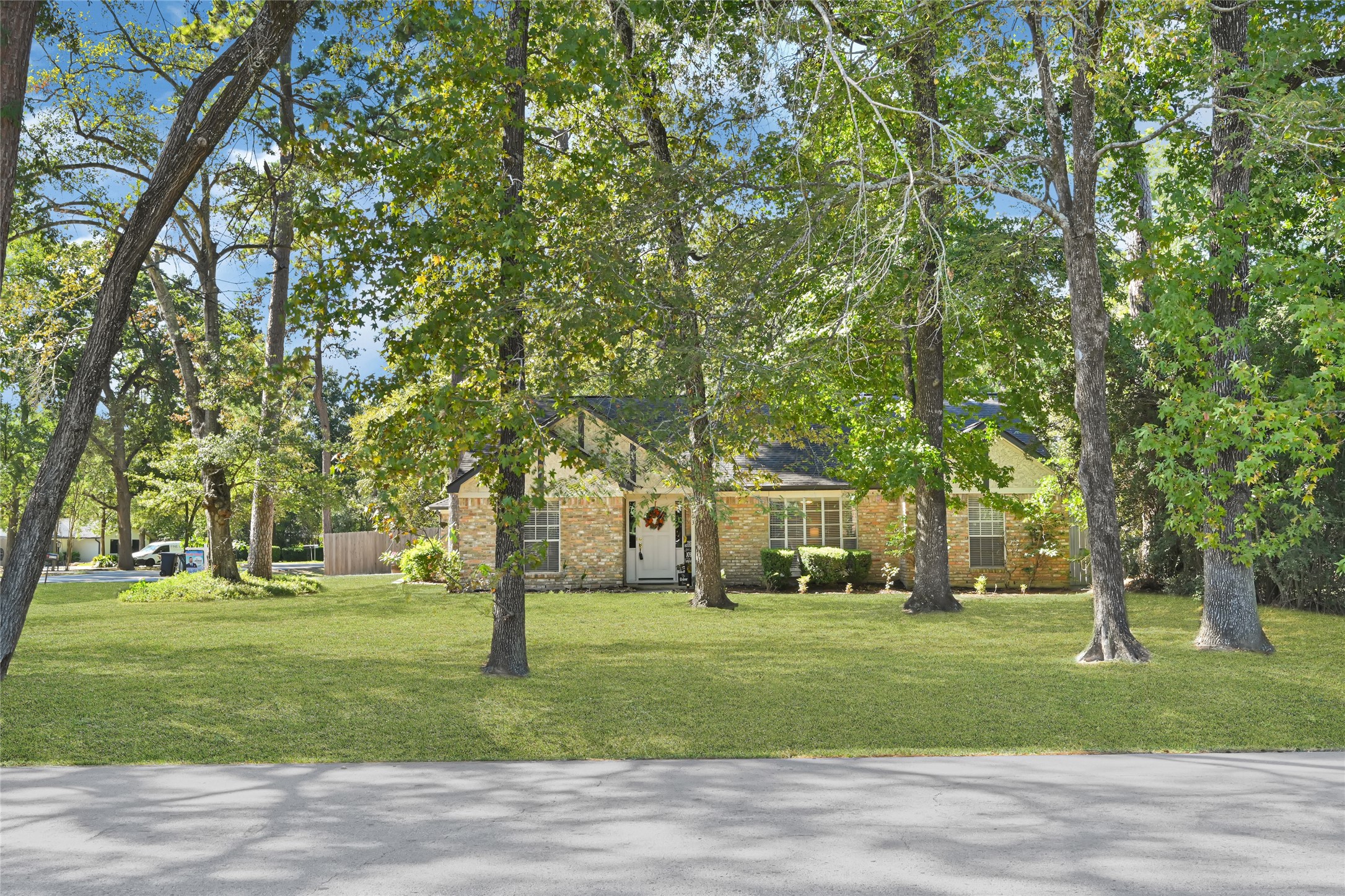 Charming brick home nestled among mature trees, offering a serene and spacious front yard.