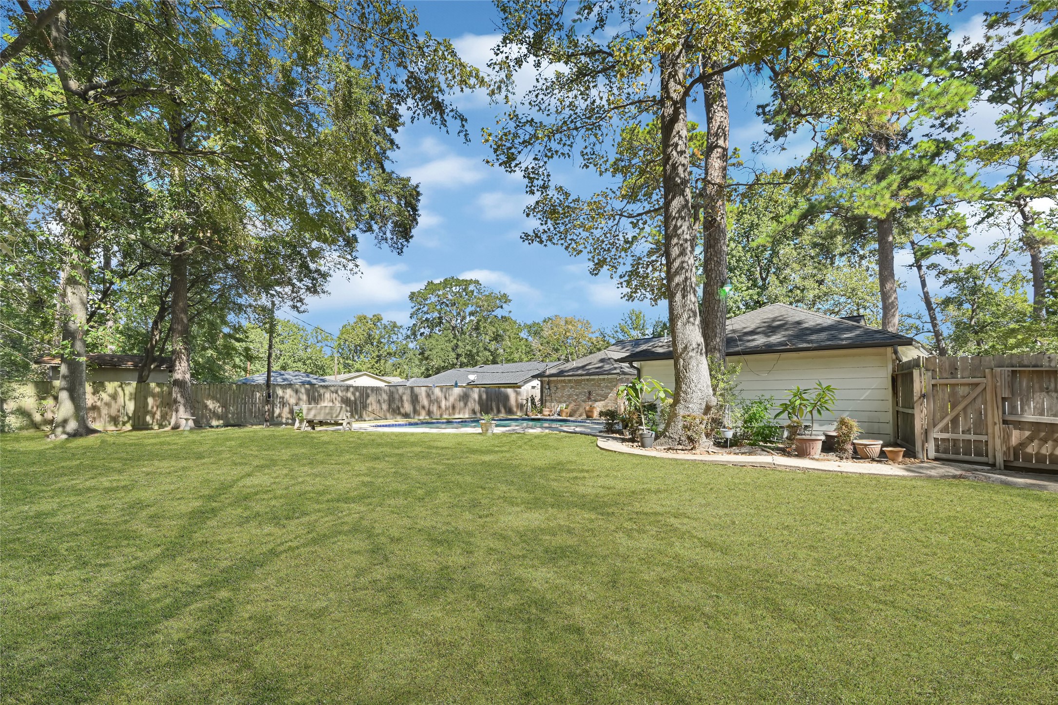 Expansive backyard featuring lush green lawn, mature trees, and a sparkling pool, perfect for outdoor relaxation and entertainment.