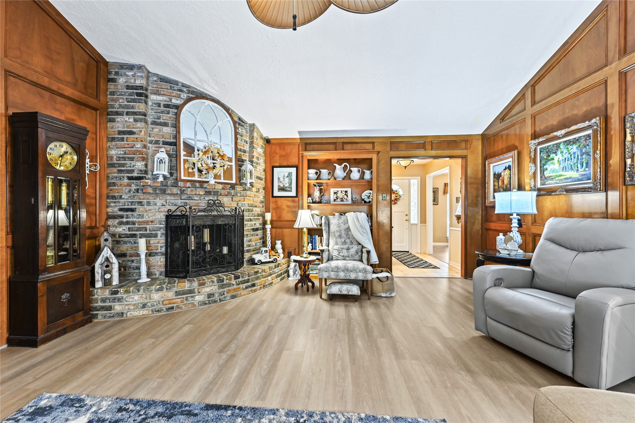 Cozy living room with rich wood paneling and a striking brick fireplace, complemented by elegant decor and comfortable seating.