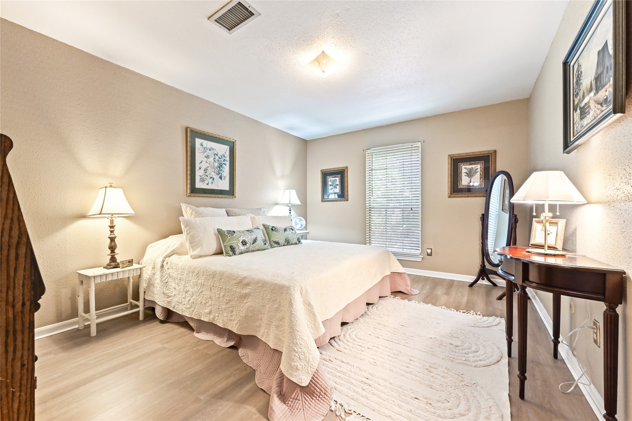 Cozy bedroom featuring soft neutral tones, elegant furnishings, and ample natural light from a large window, creating a serene and inviting atmosphere.