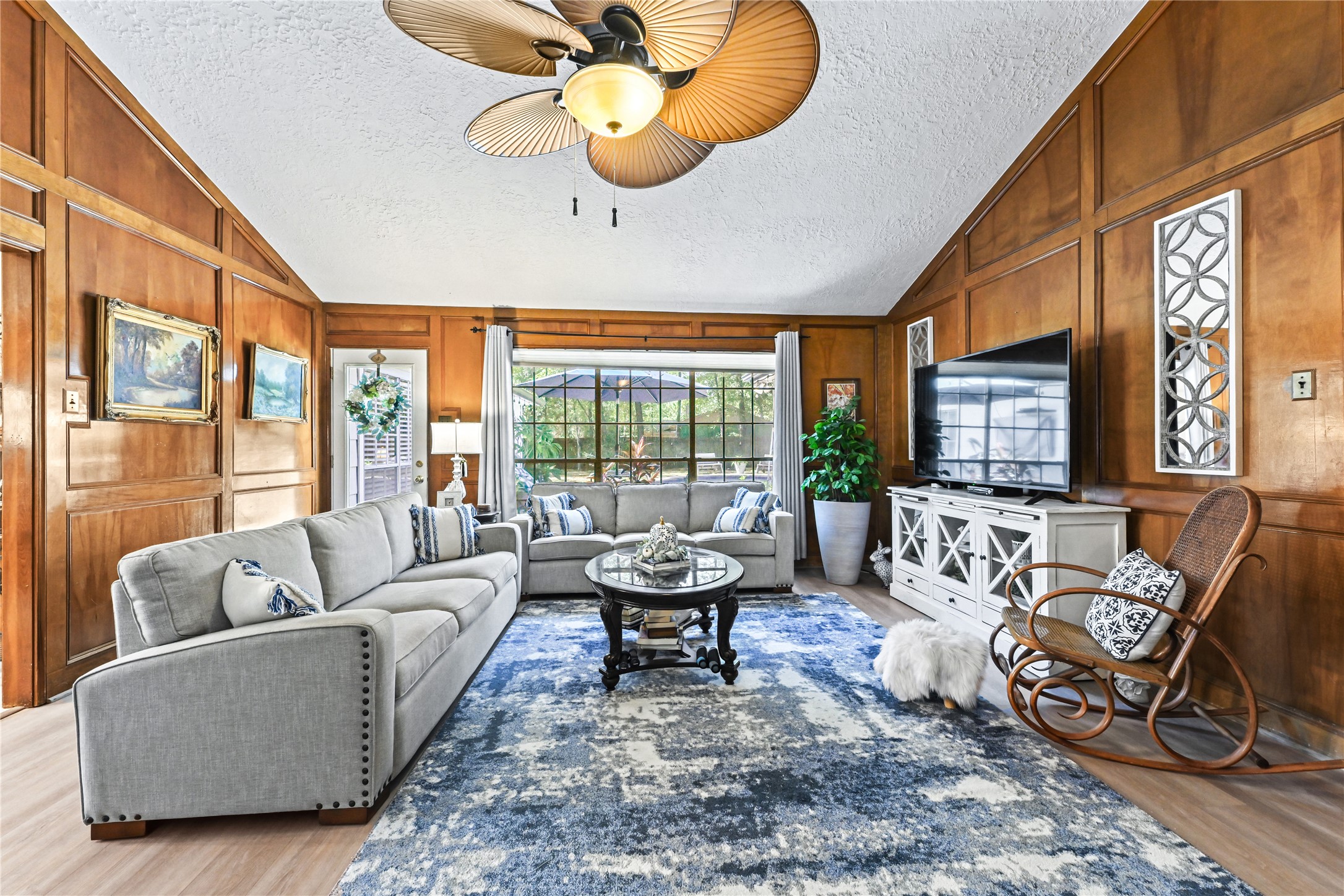 Elegant living room with rich wood paneling, plenty of natural light, and stylish furnishings including a cozy gray sofa and modern accents.