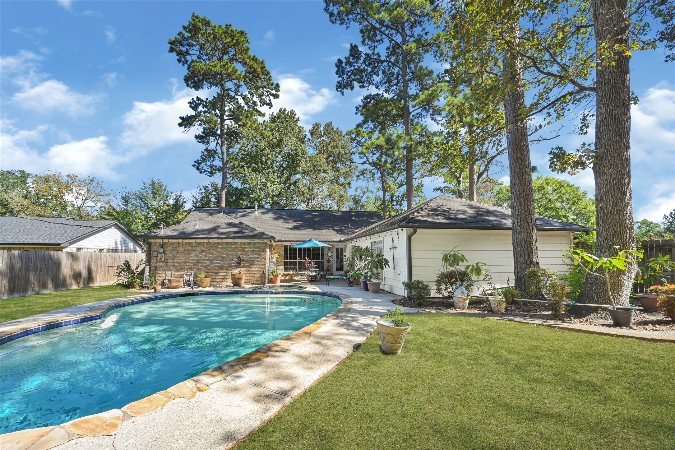 Charming backyard oasis featuring a sparkling pool surrounded by lush greenery and mature trees, perfect for relaxation and entertaining.