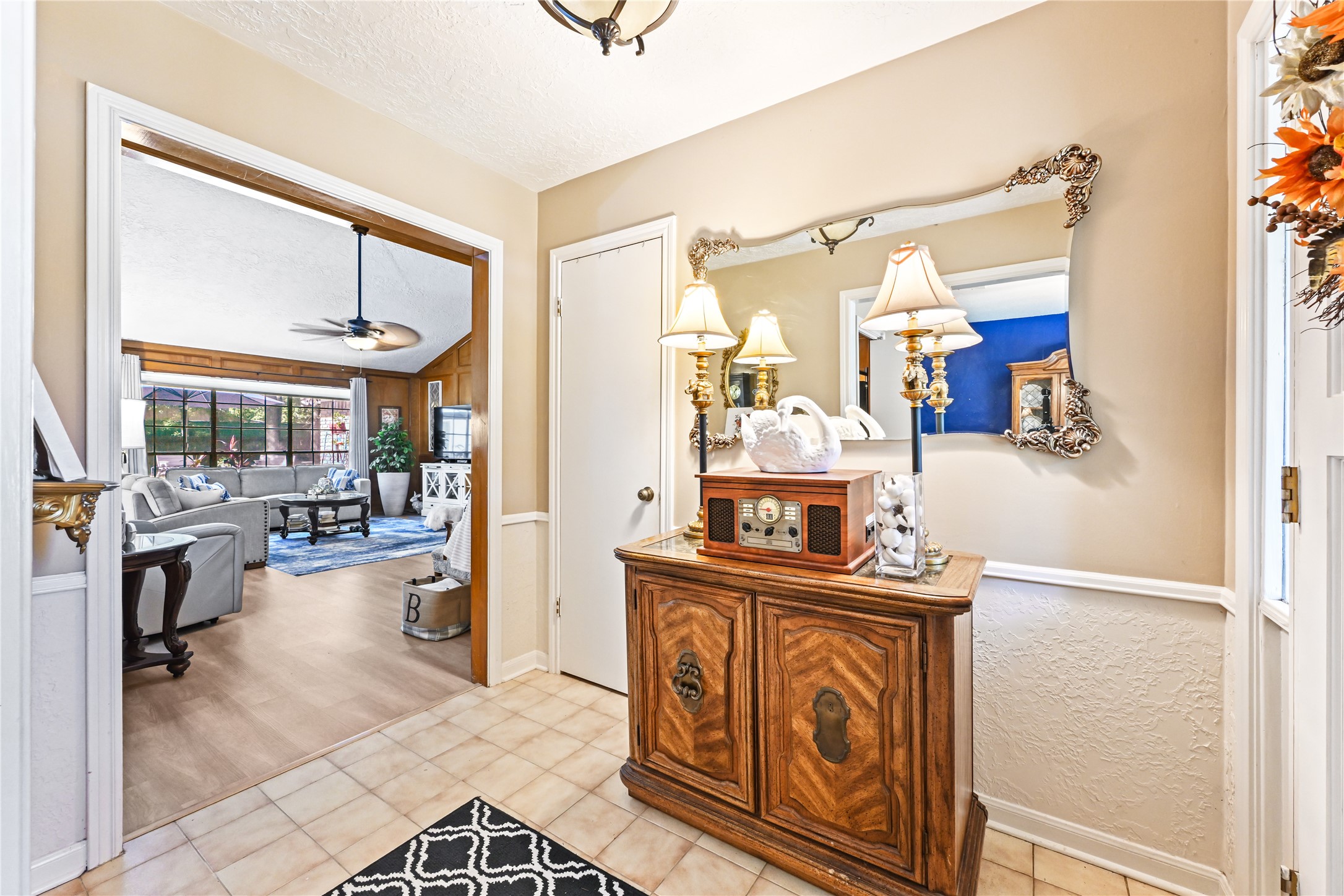 Charming entryway with elegant decor leads to a spacious living room featuring a cozy seating area, large windows, and a ceiling fan. Charming entryway with elegant decor leads to a spacious living room featuring a cozy seating area, large windows, and a ceiling fan.