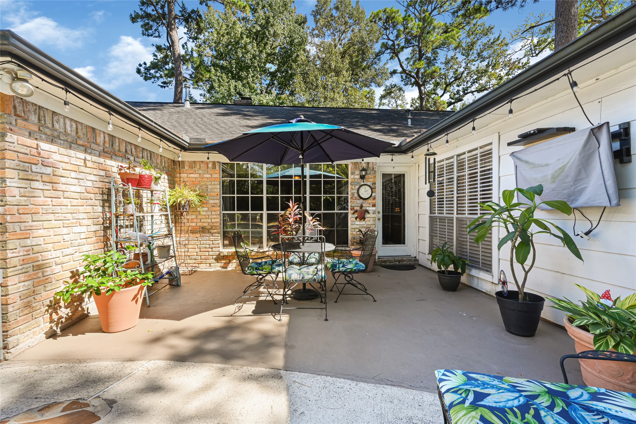 Charming outdoor patio with lush potted plants, cozy seating, and a large umbrella, perfect for relaxing or entertaining under the open sky.