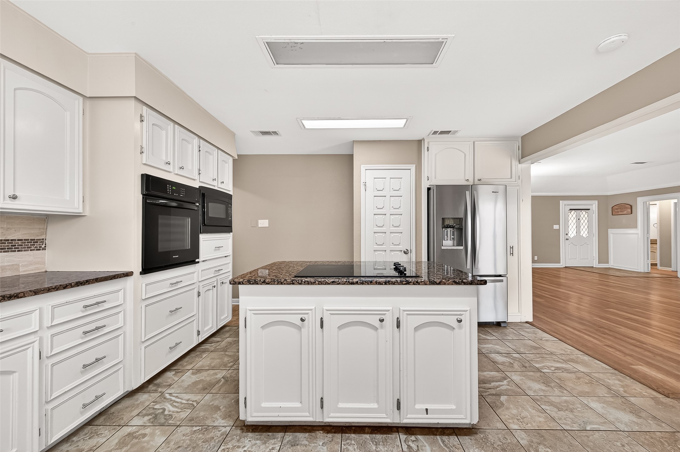 Kitchen with modern appliances, granite countertops, and ample white cabinetry. Open layout flows into a bright living area with wood flooring. Ideal for entertaining and family living.