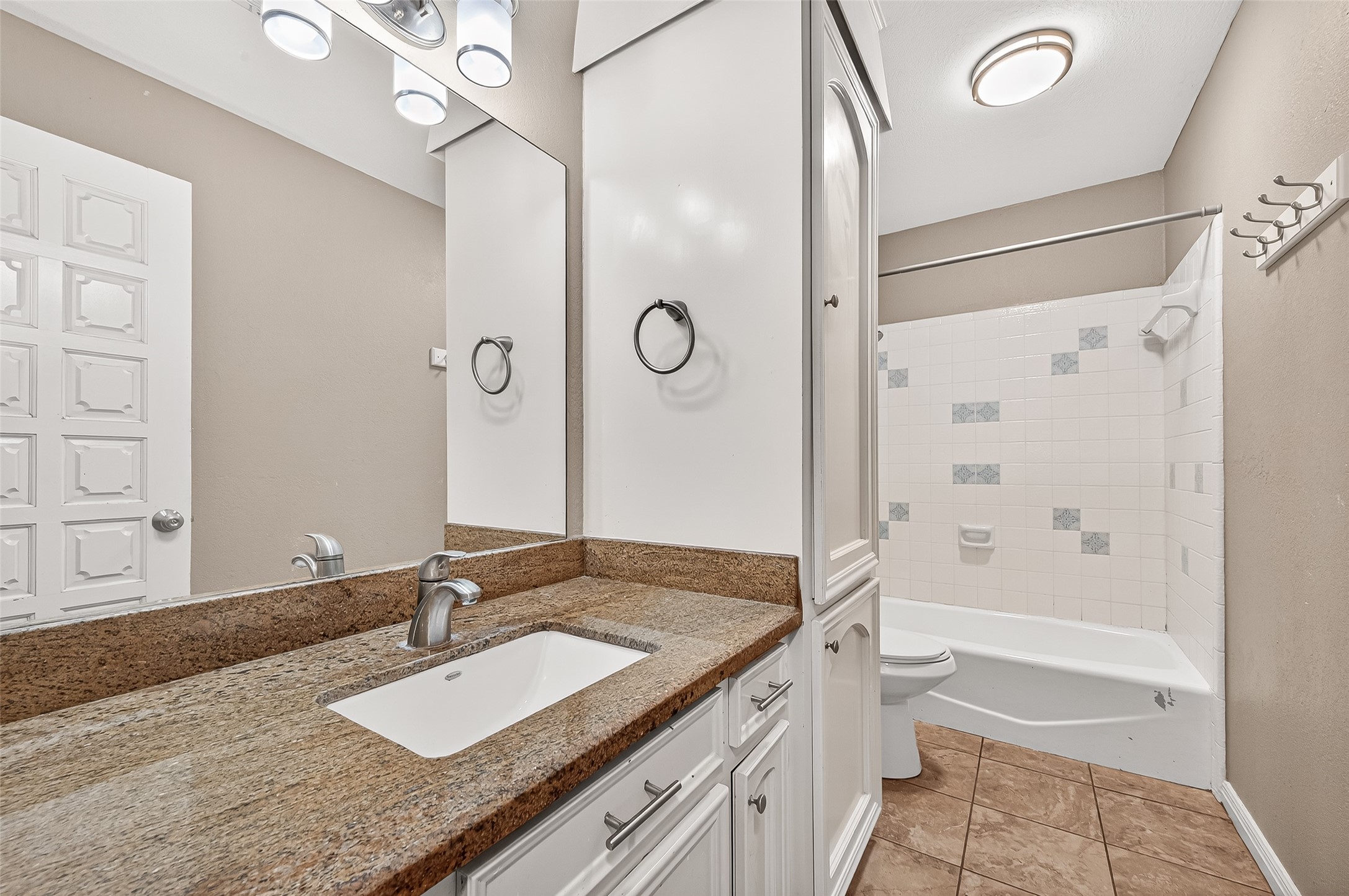 This bathroom features a granite countertop with a modern sink, ample cabinet storage, and a full bathtub with a tiled shower. The neutral color palette and bright lighting create a clean and inviting atmosphere.