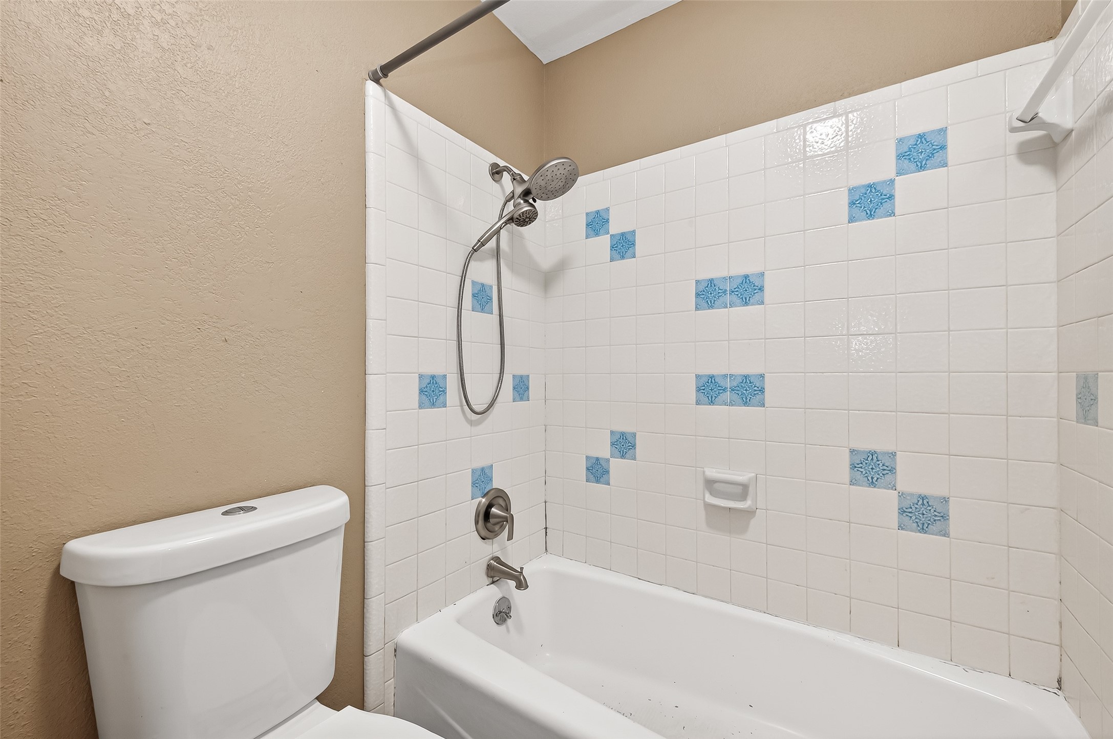 Cozy bathroom featuring a bathtub with a showerhead, accented by white tiles with blue patterns. Neutral wall color complements the clean, functional design.
