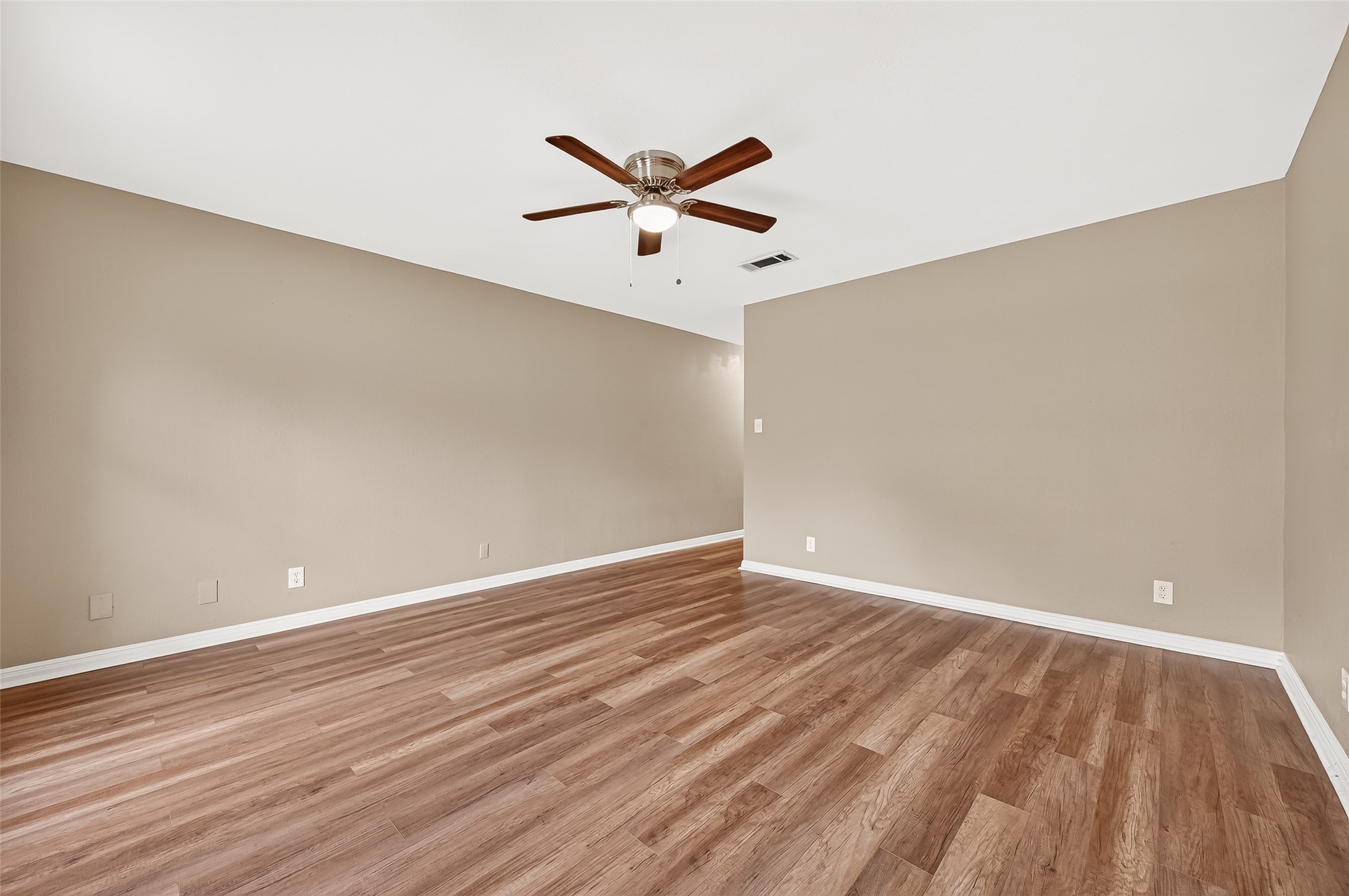 This photo showcases a spacious room with warm-toned walls and wood flooring. It features a ceiling fan and ample natural light, offering a cozy and inviting atmosphere ideal for various uses.
