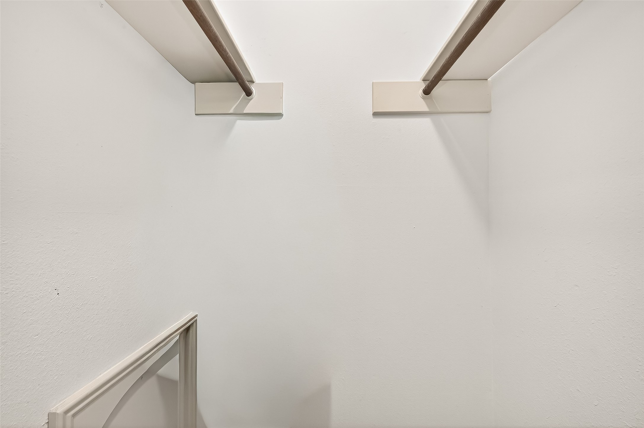 This image shows a simple, white walk-in closet with dual hanging rods, offering ample space for clothing storage.