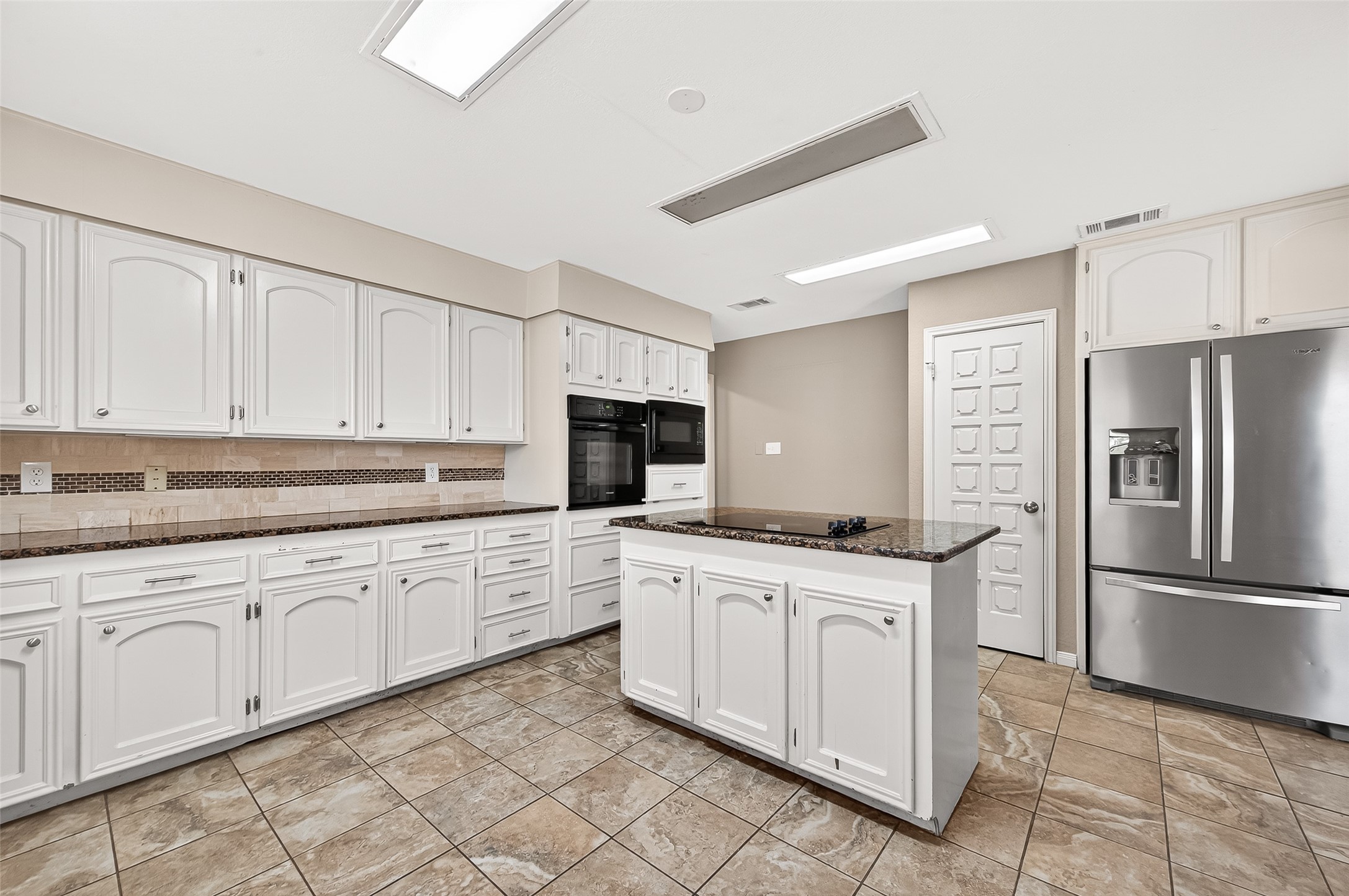 Kitchen with modern appliances, ample white cabinetry, and a central island. Features include tiled flooring, granite countertops, and recessed lighting for a bright, welcoming atmosphere.